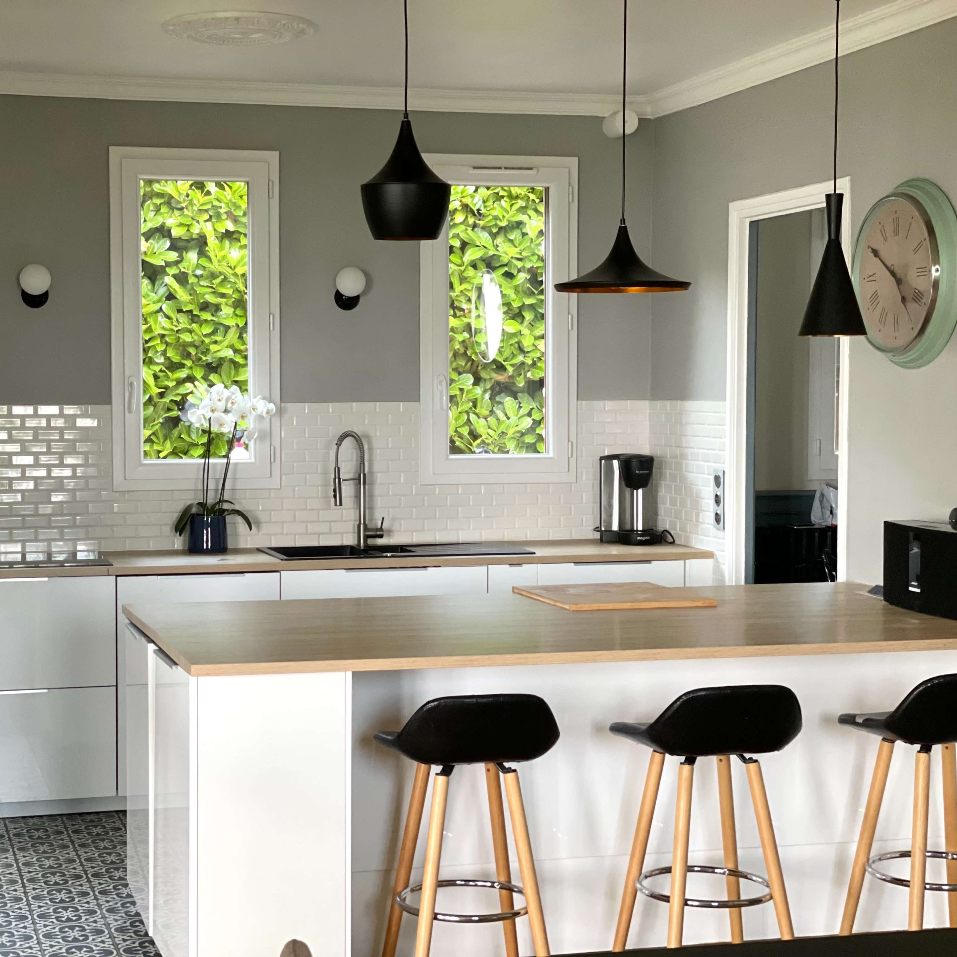 A modern kitchen features a central island with bar stools, white cabinetry, and large windows letting in natural light.