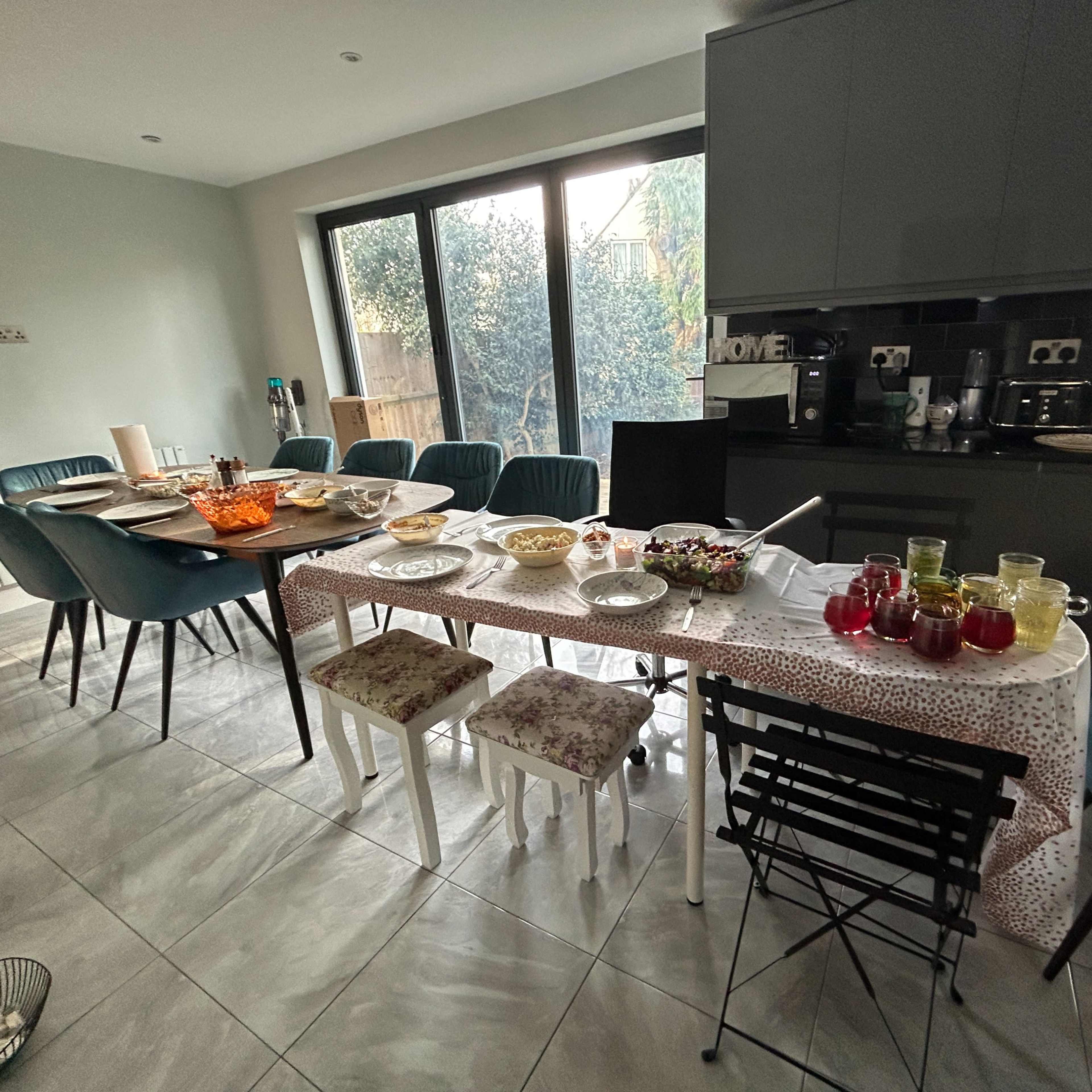 A dining table set with various dishes and drinks is surrounded by chairs in a modern kitchen.