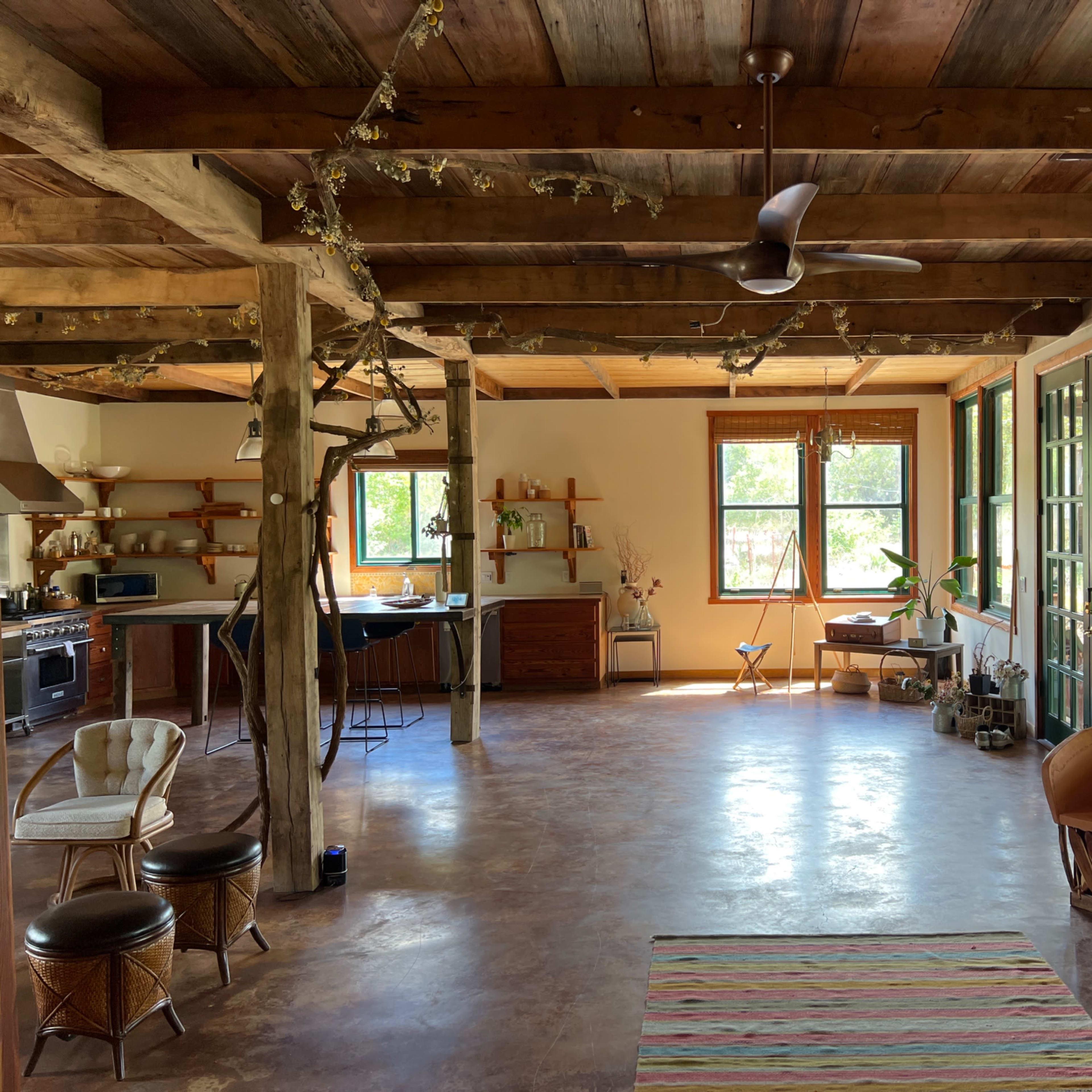 A spacious, open-concept living area with wooden beams, large windows, and minimalist furnishings.