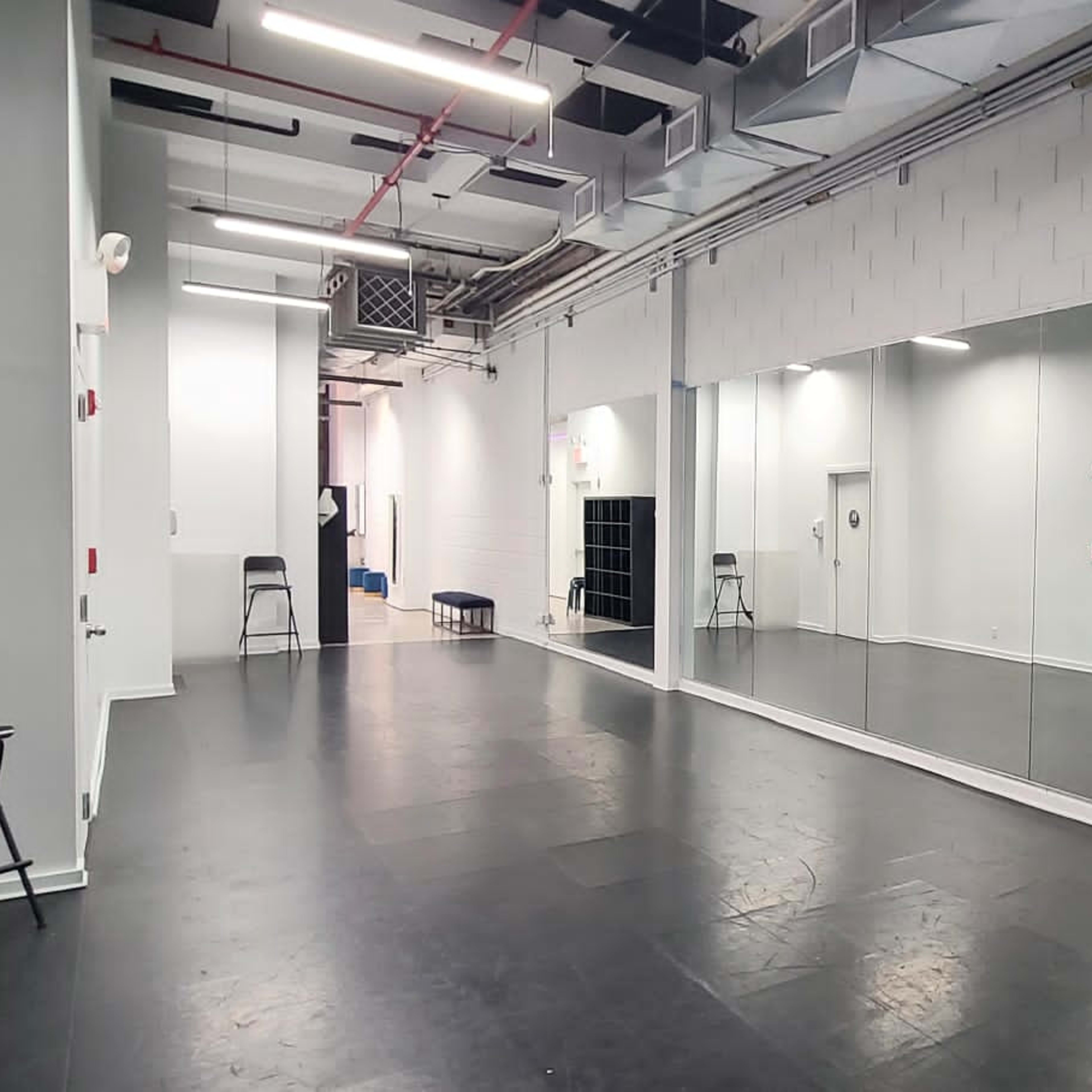 A spacious, empty dance studio featuring a large mirrored wall and black flooring.