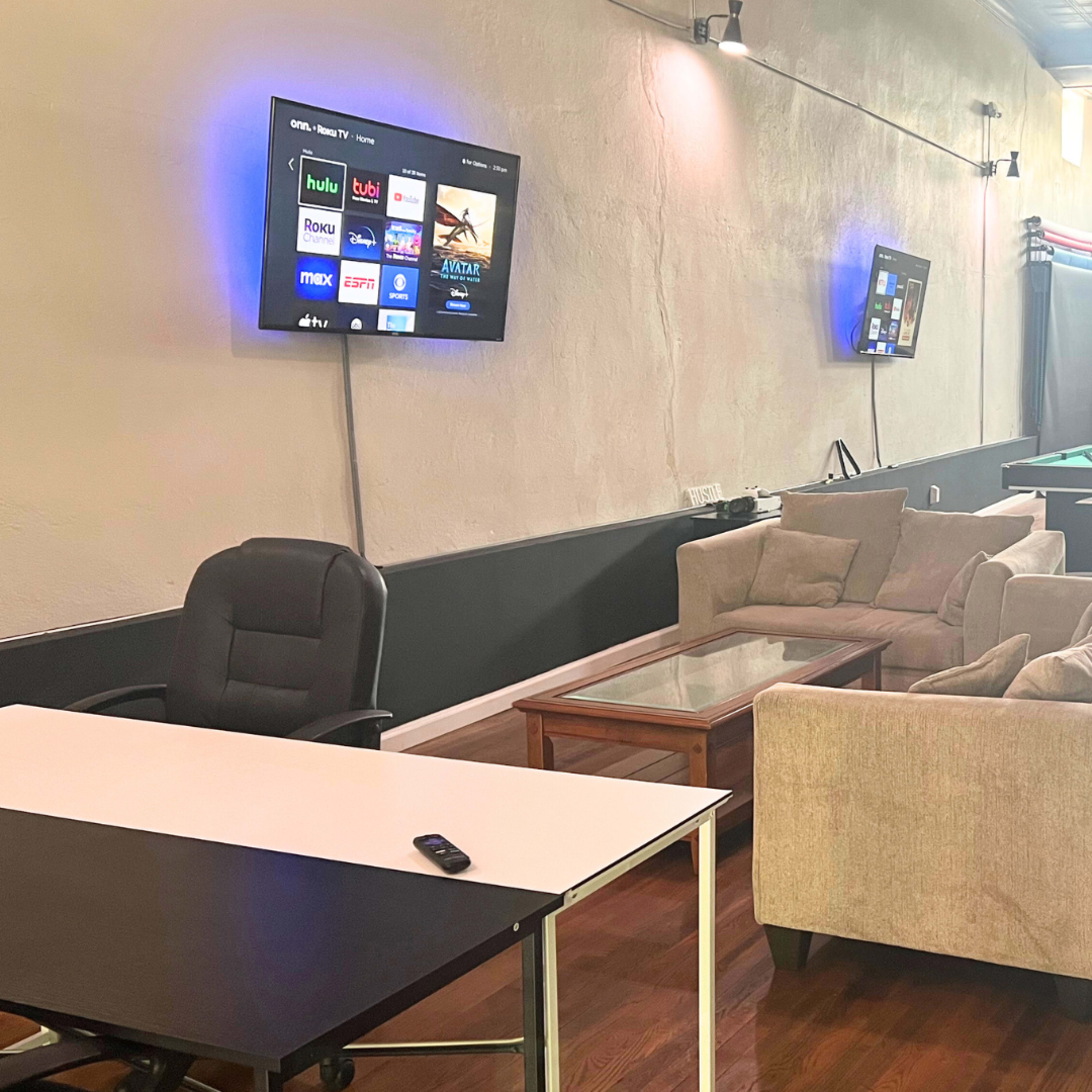 A casual lounge area with a couch, coffee table, and desk, accompanied by a television on the wall and a pool table in the background.