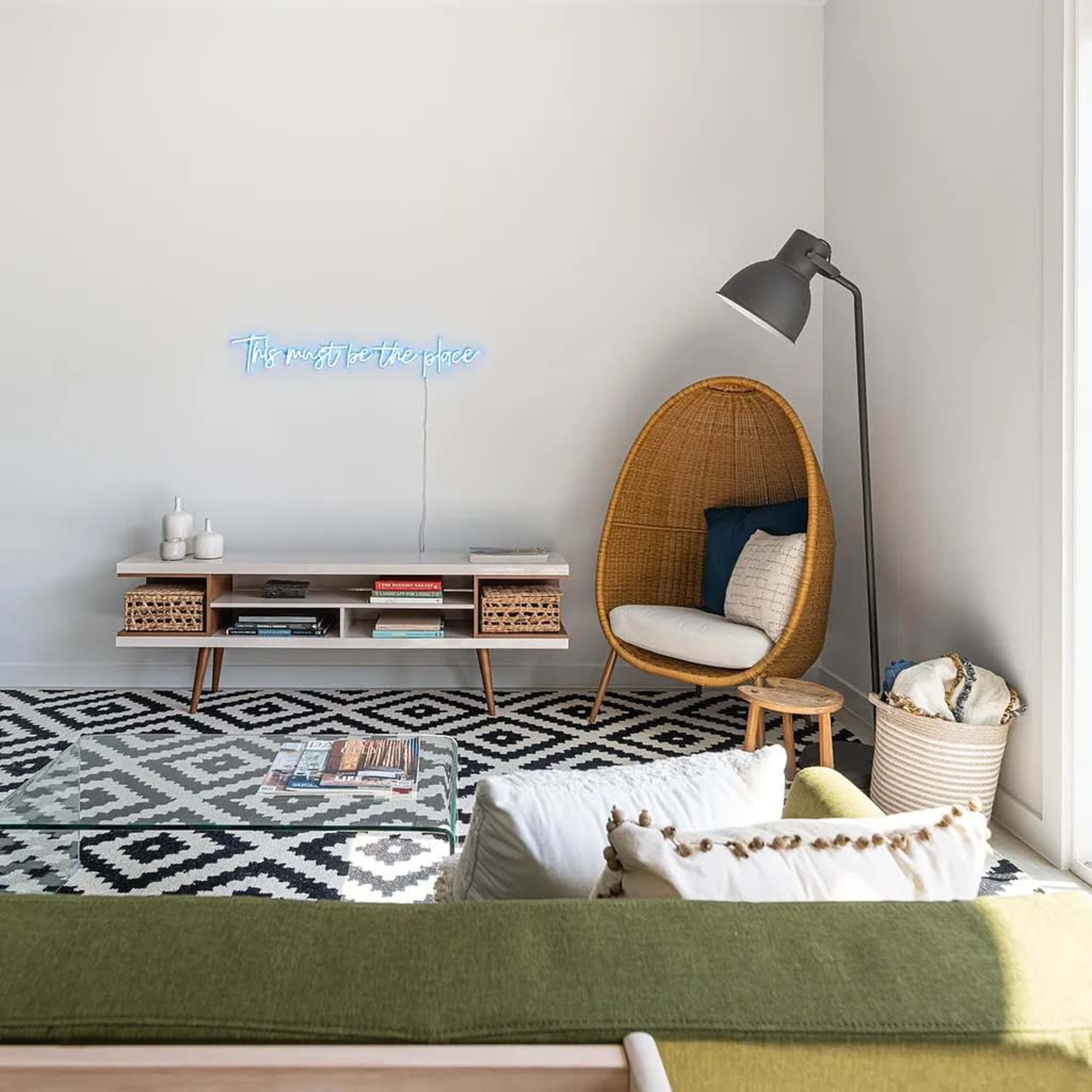 A modern living room with a patterned rug, a green sofa, a blue armchair, a rattan chair, and a minimalist coffee table.