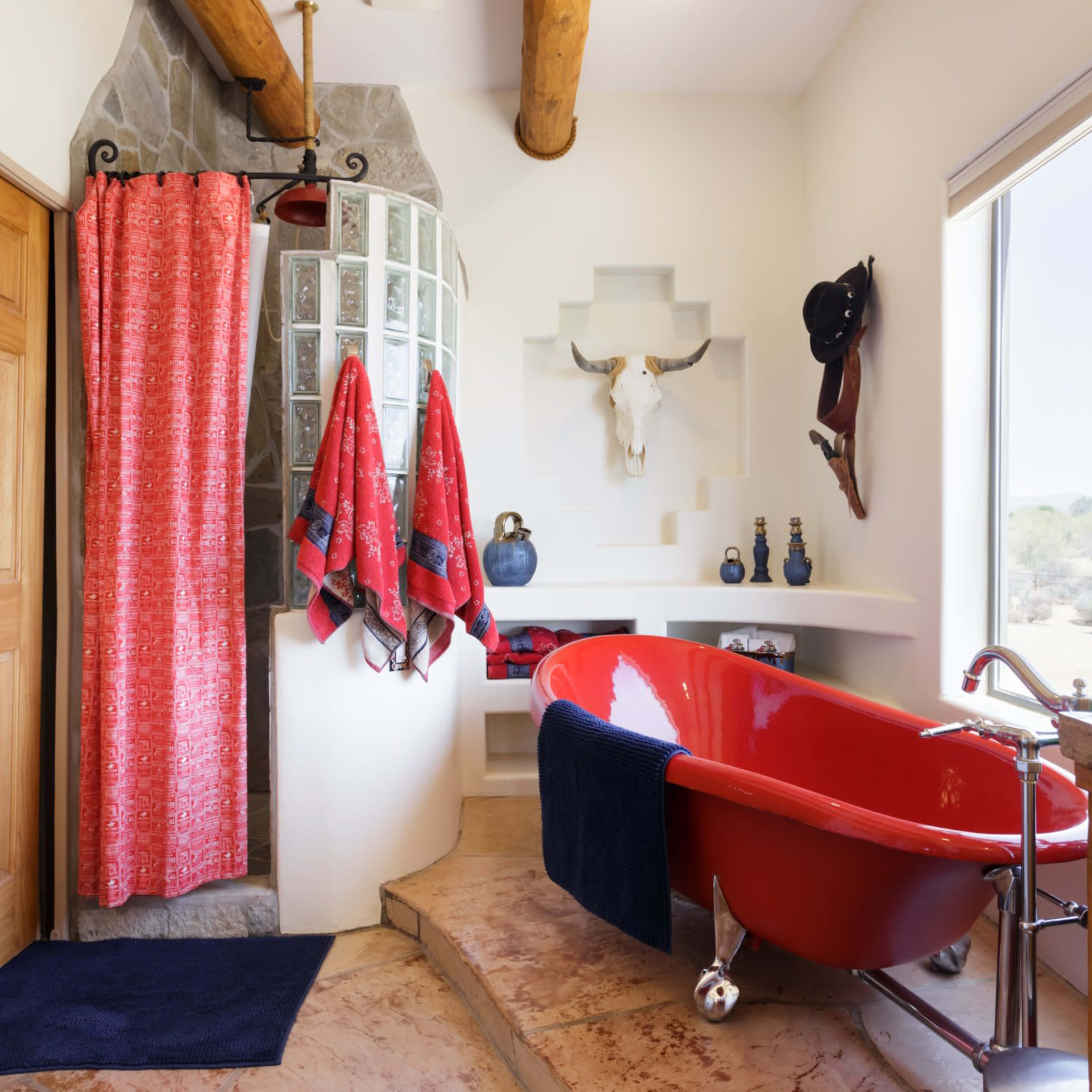A modern bathroom featuring a red bathtub, a circular glass shower, wooden cabinetry, and large windows with a view of the outdoors.