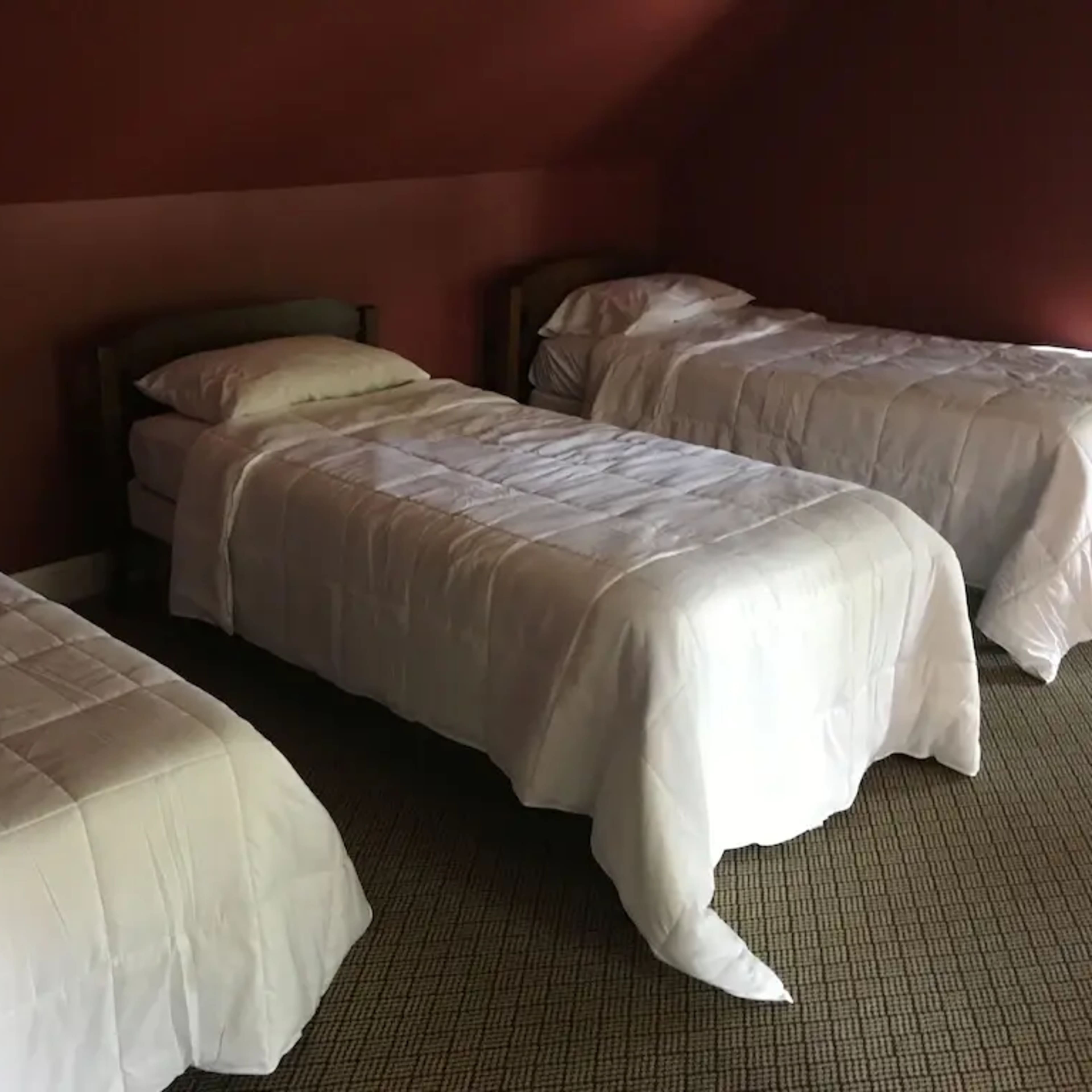 A room with three beds covered in white linens against a reddish-brown wall.