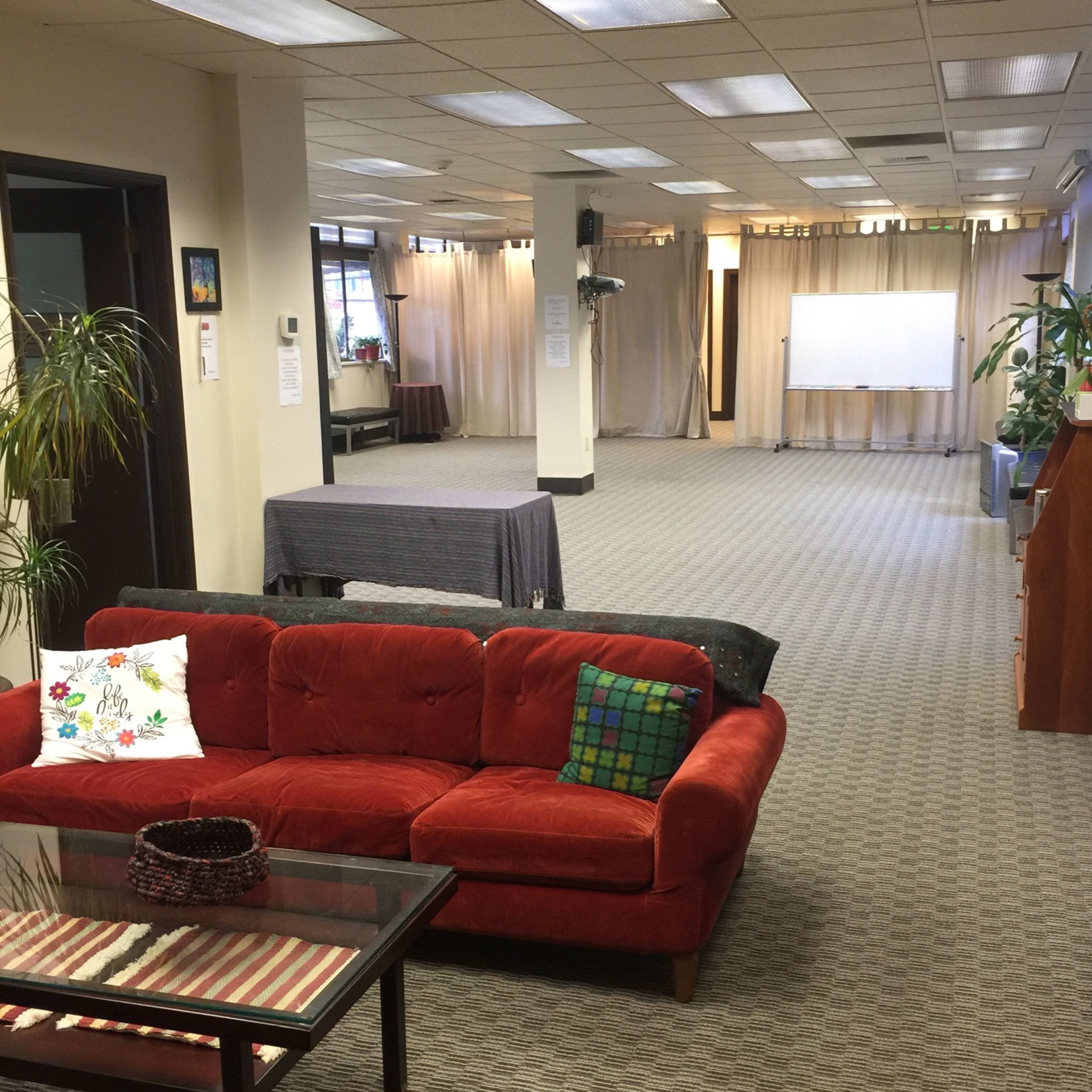 A spacious room with a red sofa, several plants, and a large screen at one end.
