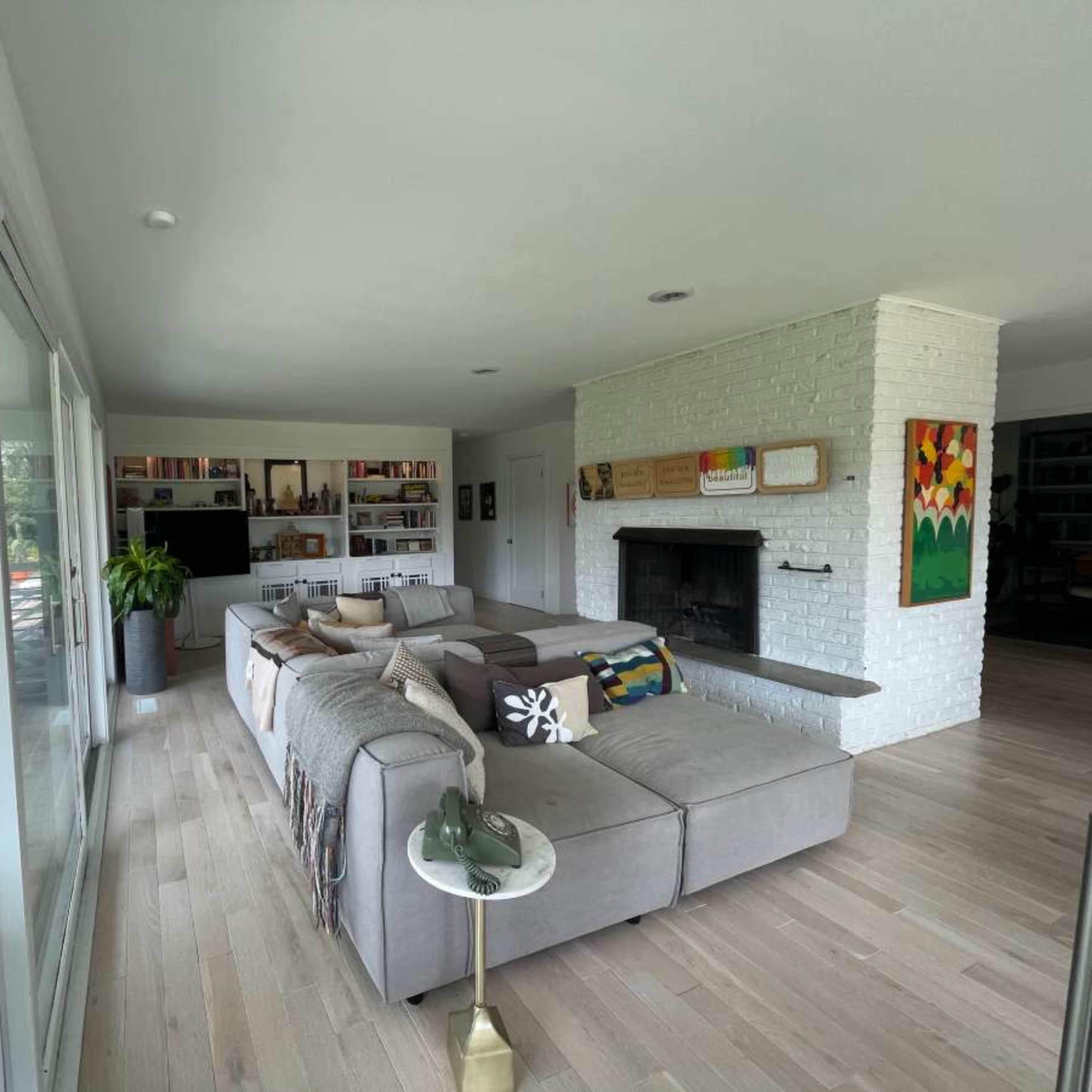 A modern living room features a large sectional sofa, a white brick fireplace, and a view of the outdoors through large glass doors.