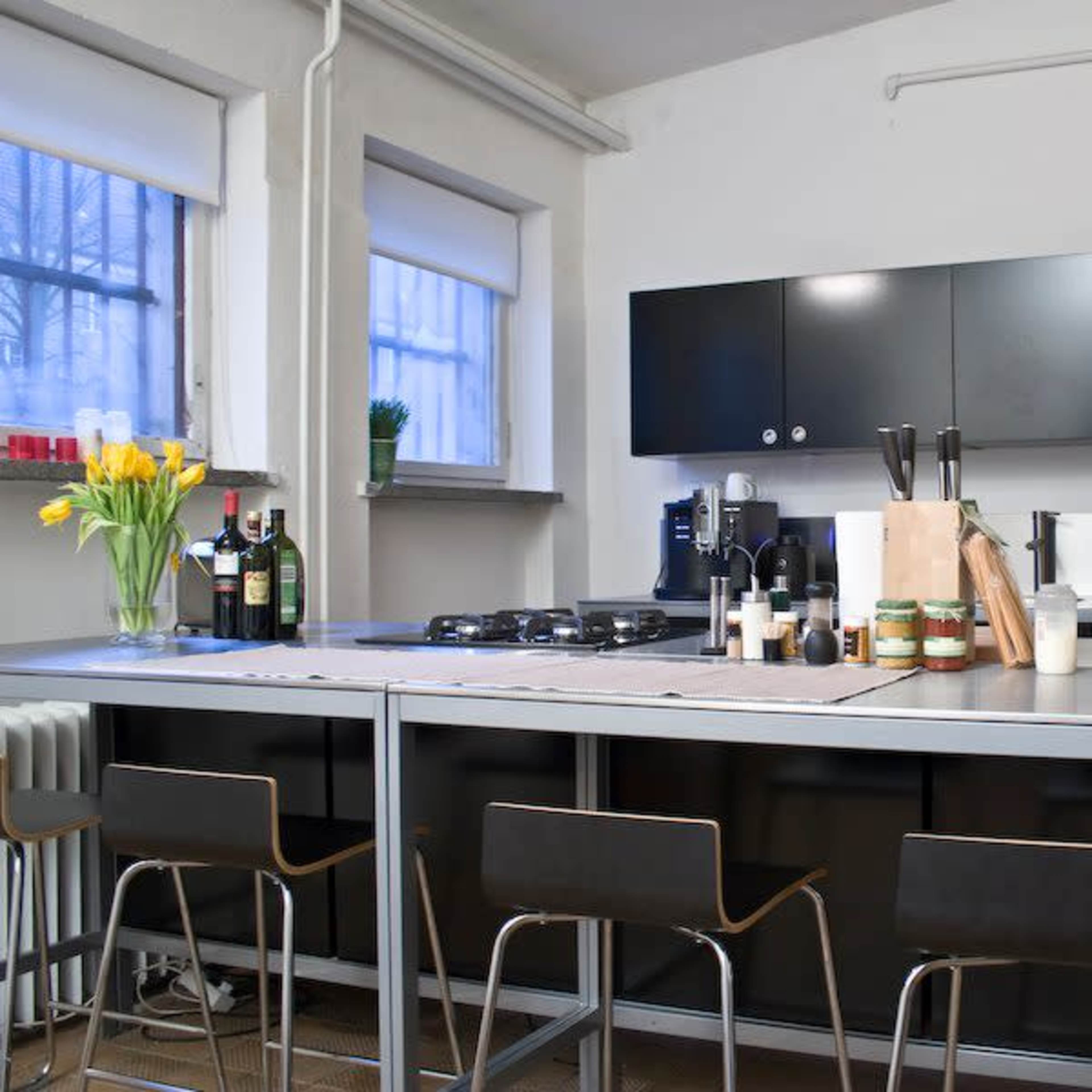 A modern kitchen features a central island with bar stools, black cabinetry, and stainless steel appliances, along with decorative items like flowers and jars on the countertop.