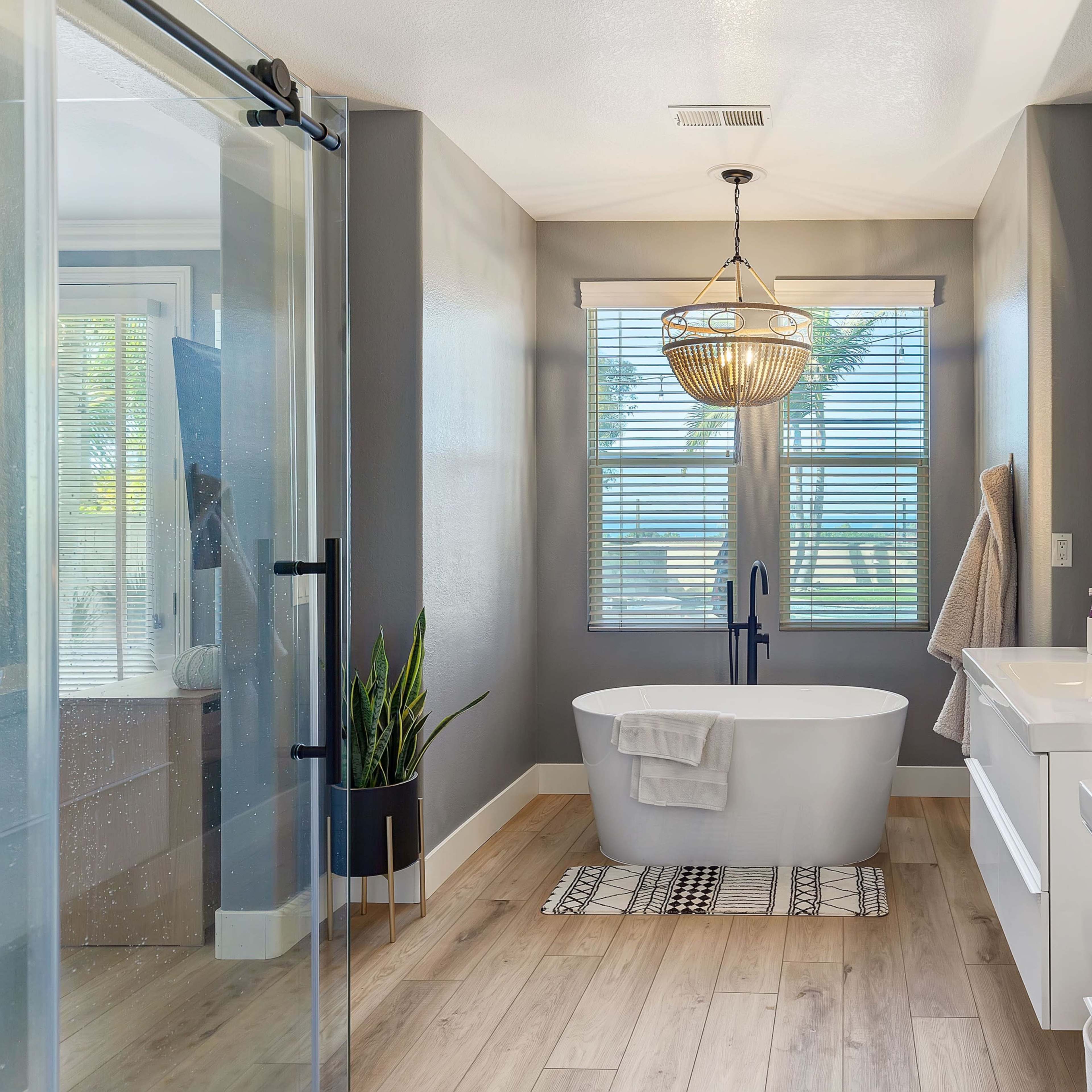 A modern bathroom featuring a freestanding bathtub, double vanities with sinks, large windows, and a walk-in shower.