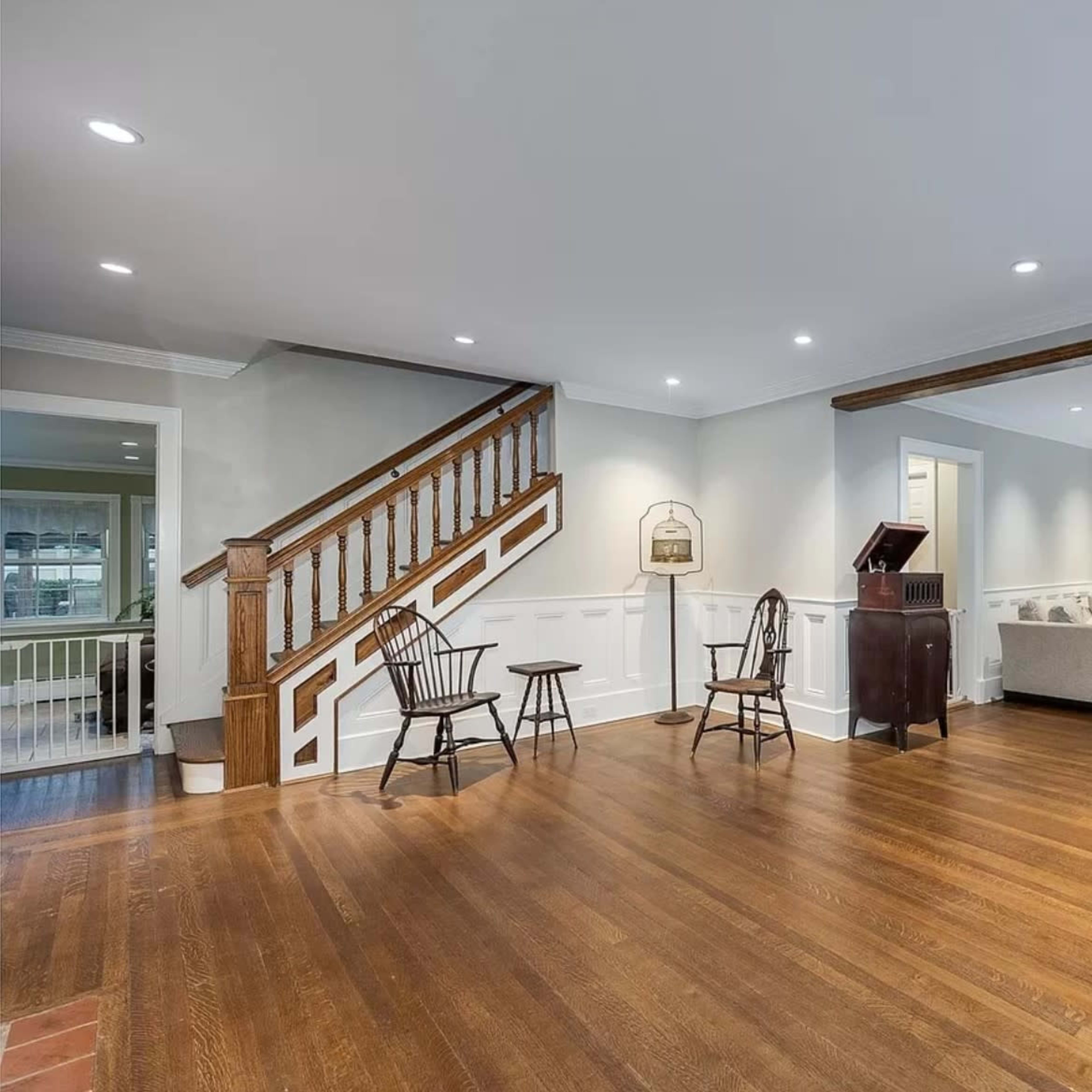 A spacious living room with hardwood flooring, a staircase, and a mix of seating arrangements including chairs and a sofa.