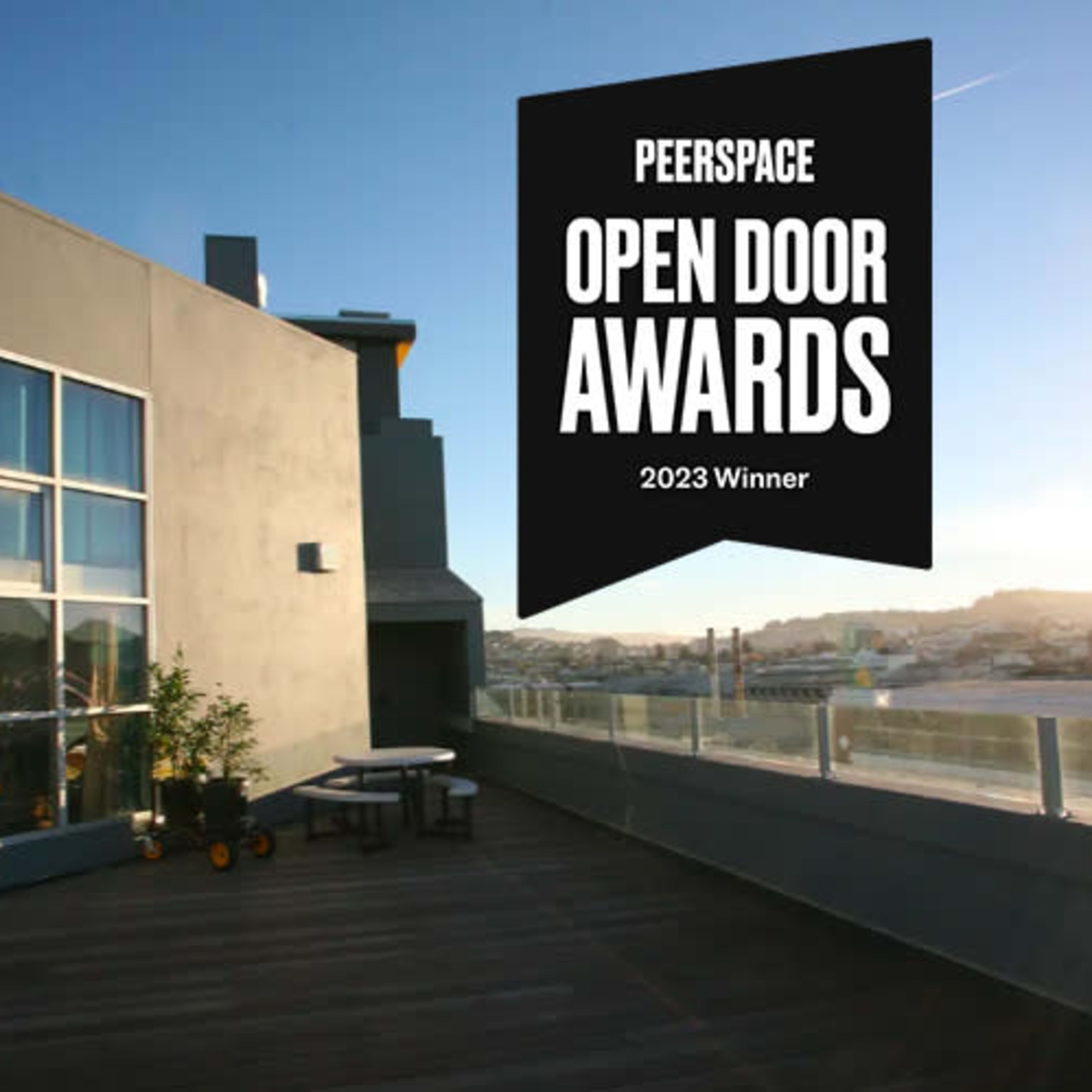 A modern rooftop space features large windows and a wooden deck, with a banner indicating it won the 2023 Peerspace Open Door Awards.