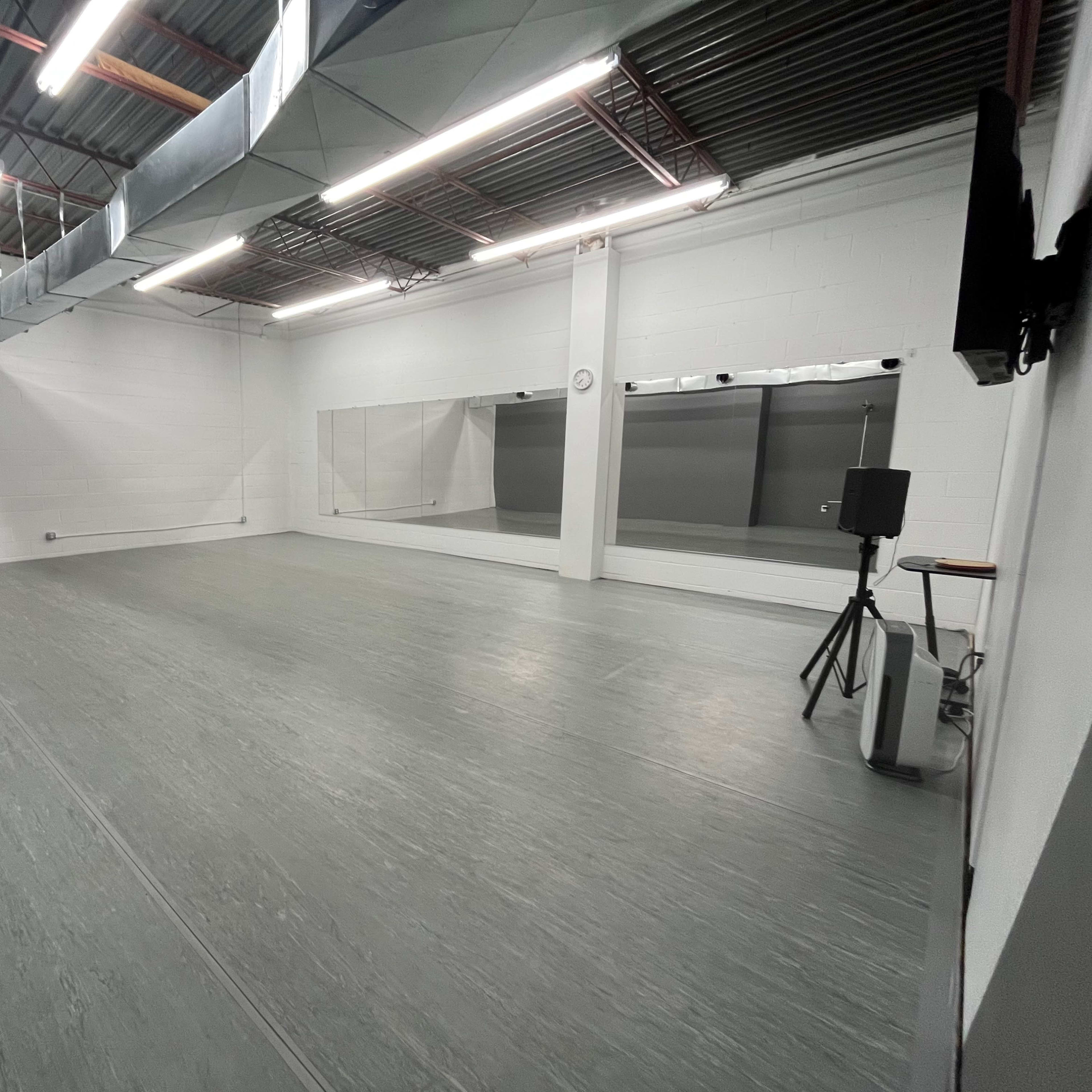A spacious, empty studio with gray flooring, white walls, and large mirrors along one side.