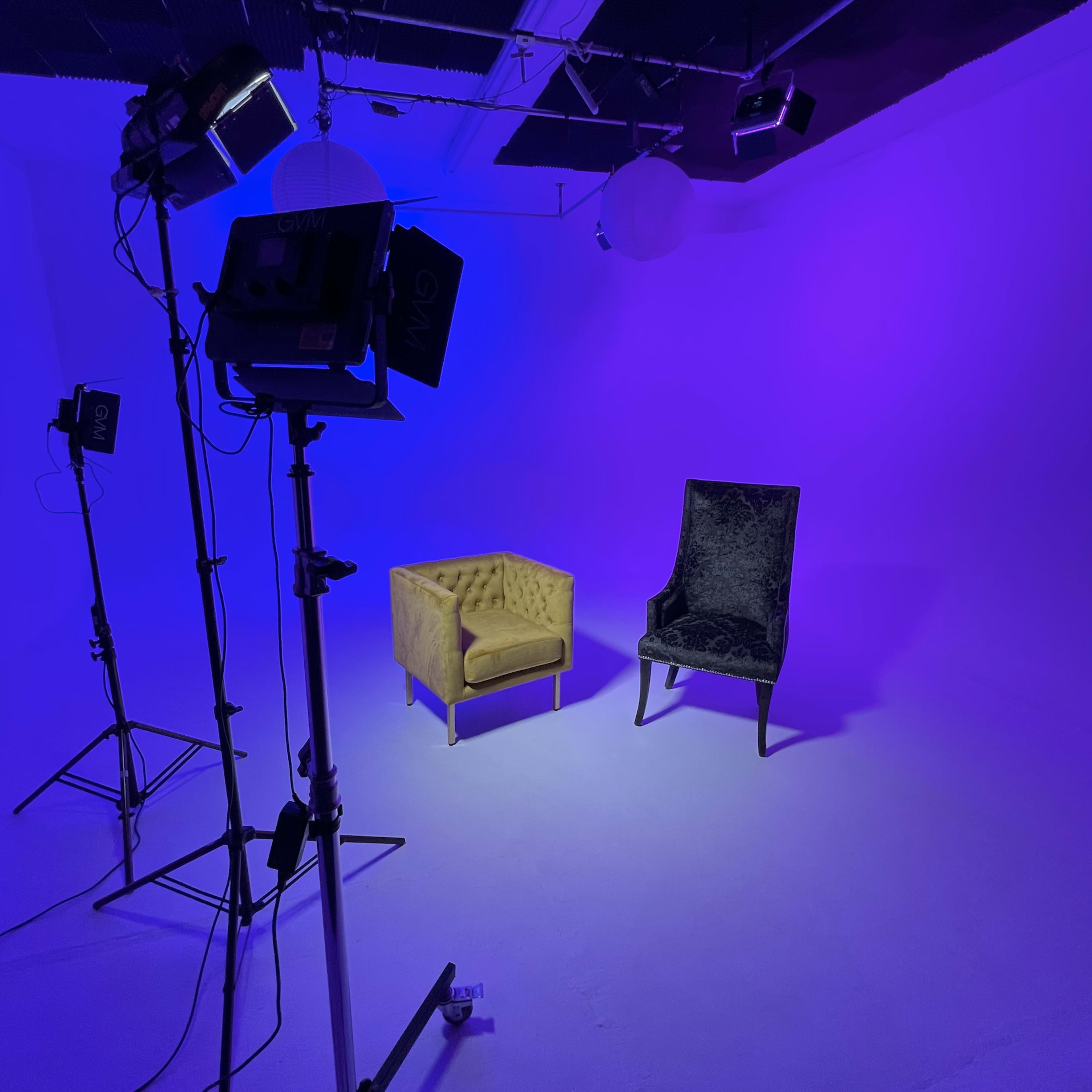 A studio setup features a yellow tufted sofa and a black upholstered chair on a purple-lit background.