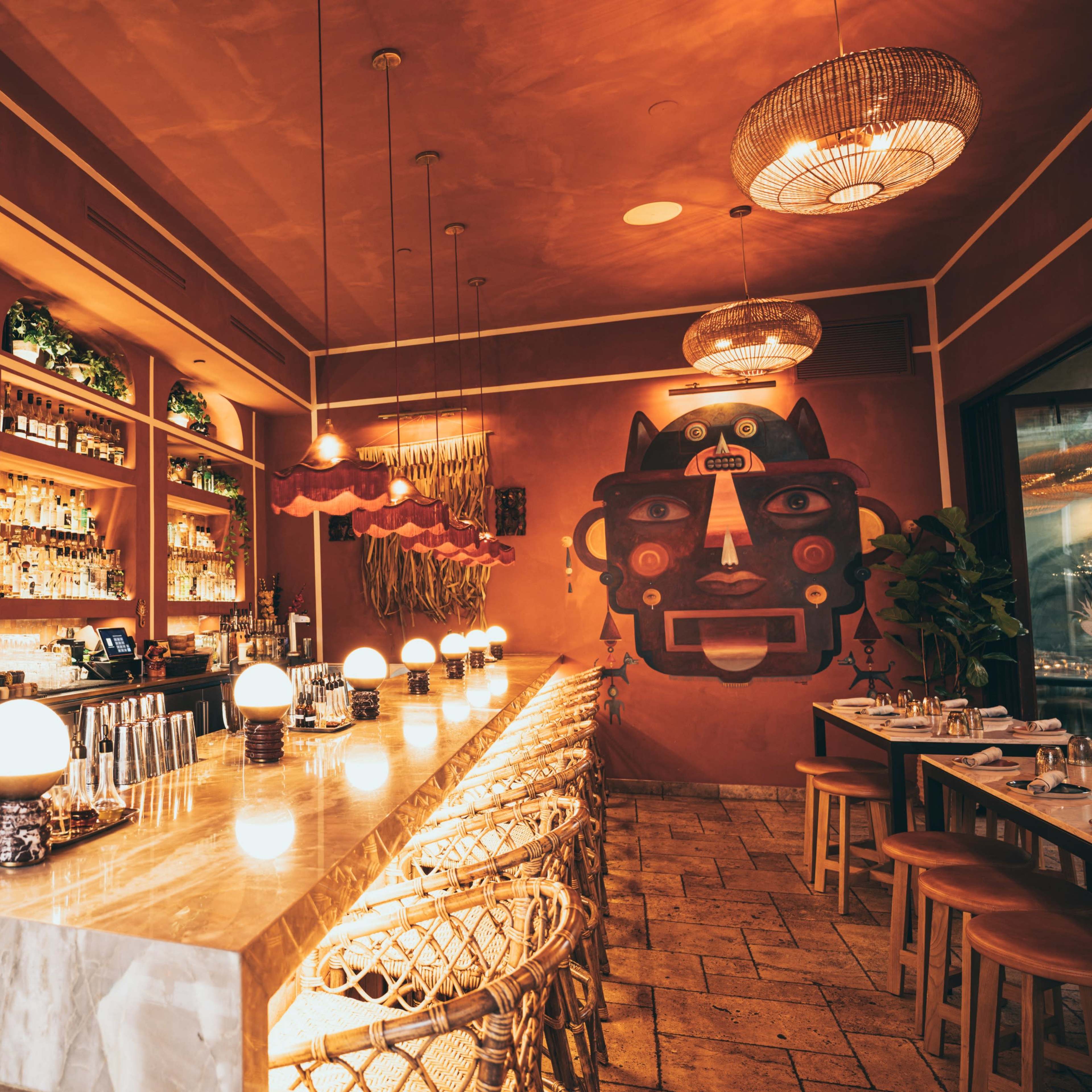 A stylish bar area in a restaurant, featuring a long marble counter, shelves stocked with various bottles, and decorative lighting fixtures.