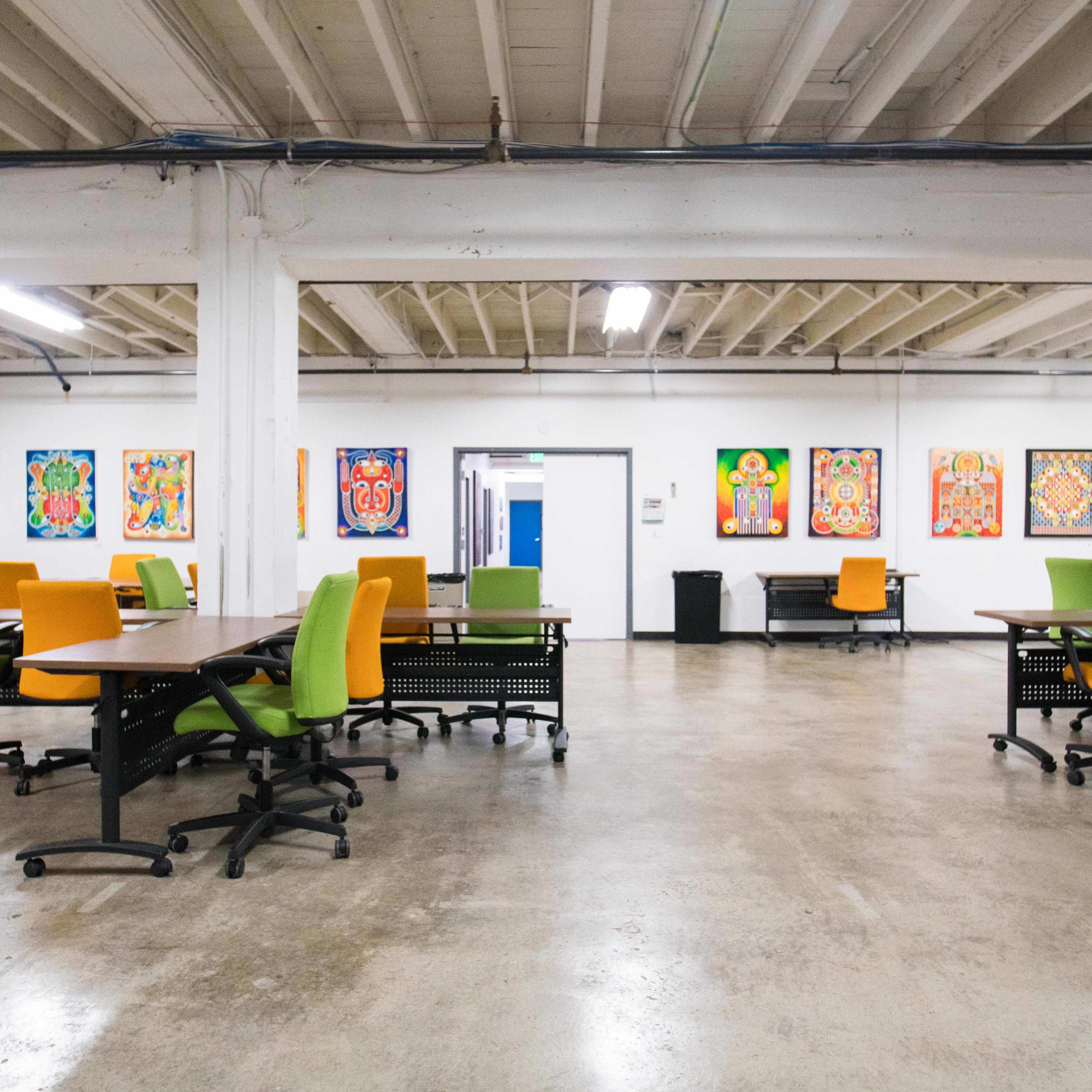 An office space with several colorful chairs and tables arranged in an open area, featuring artwork on the walls.