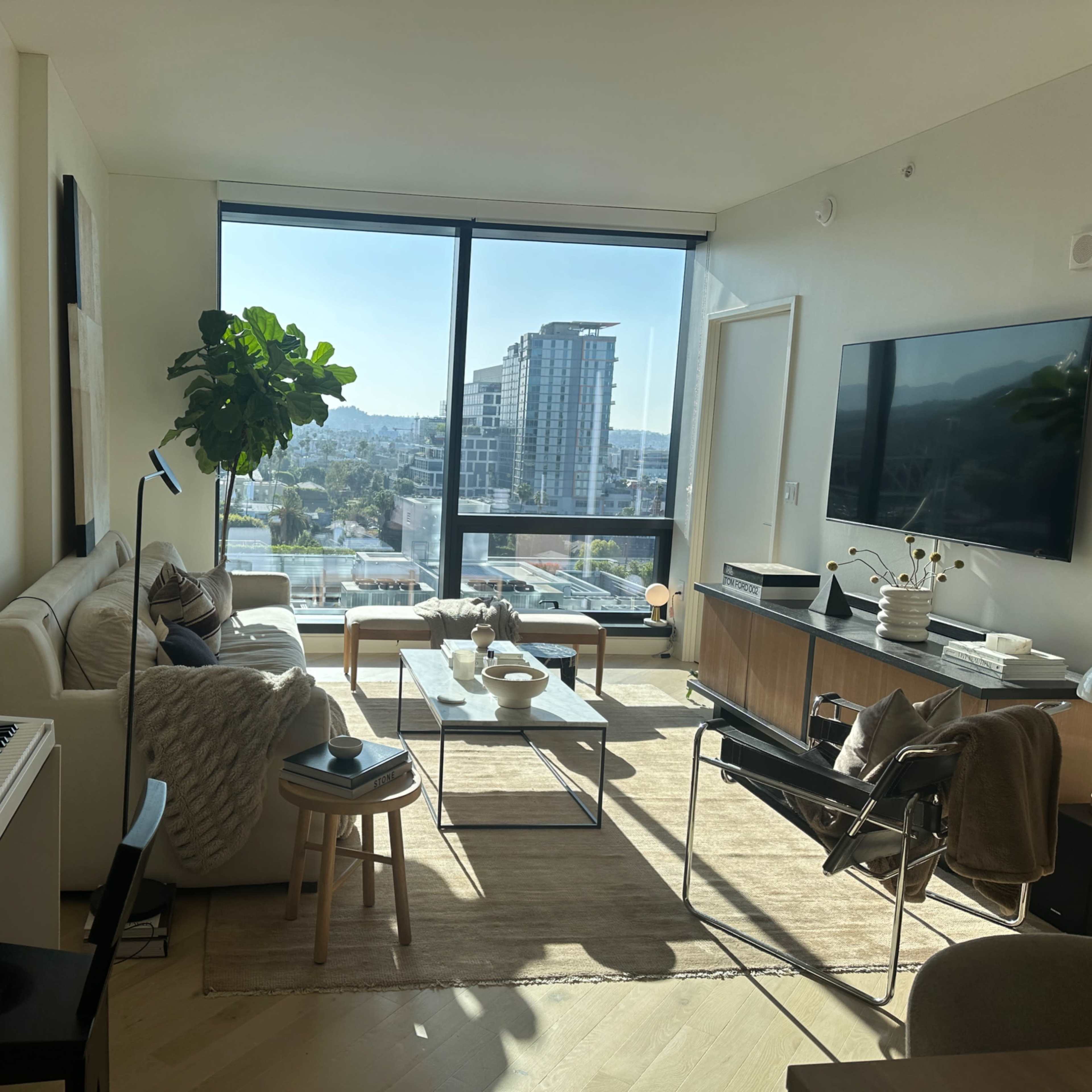 A modern living room with a large window overlooking a cityscape, a sofa, a coffee table, a keyboard, and various decorative elements.