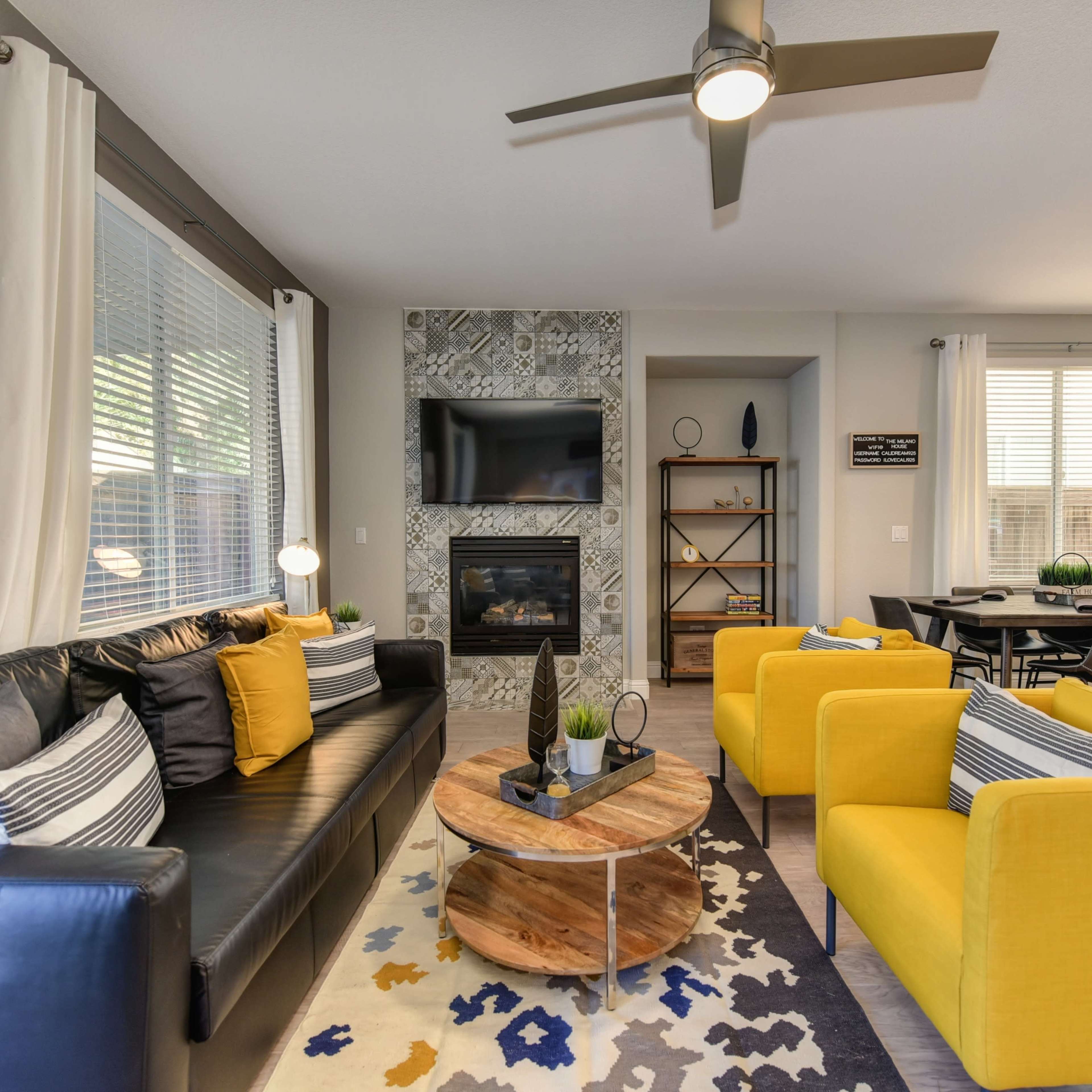 A modern living room with a black sofa, two yellow armchairs, a round wooden coffee table, and a fireplace, complemented by decorative pillows and a rug.