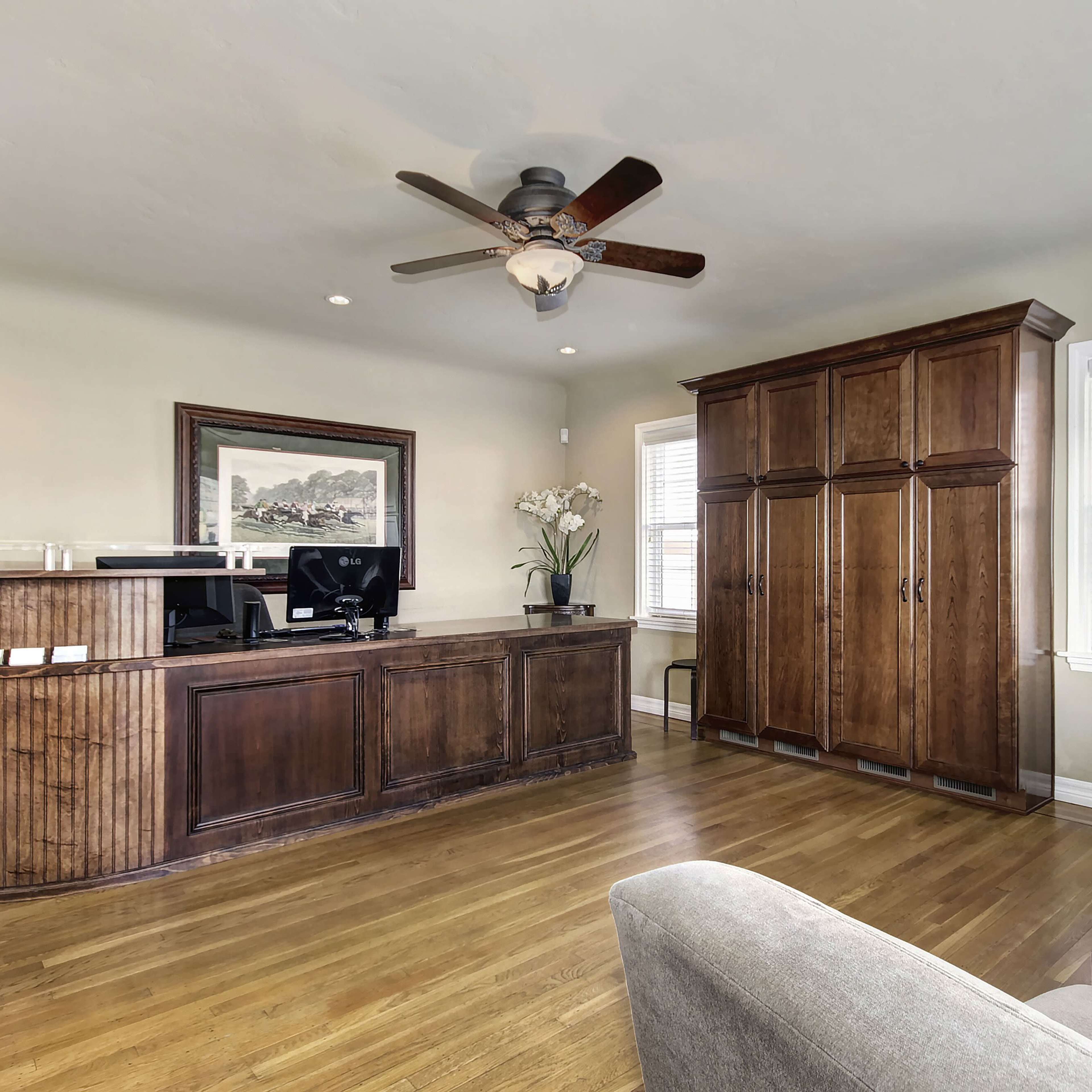 A reception area with a wooden front desk, a large storage cabinet, and seating arrangements, all set against a neutral wall color.