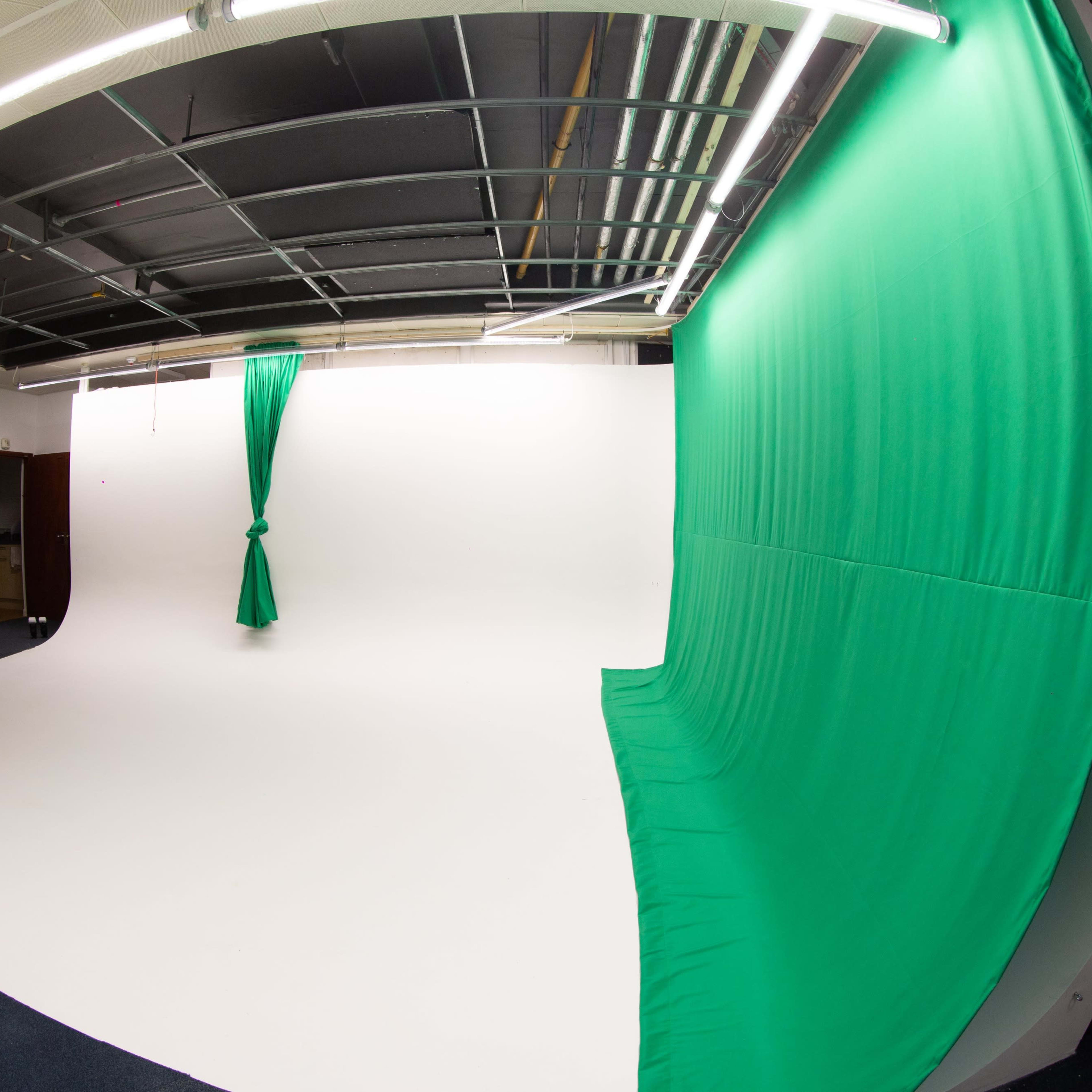 A photography studio featuring a white backdrop and a green curtain draped on one side.