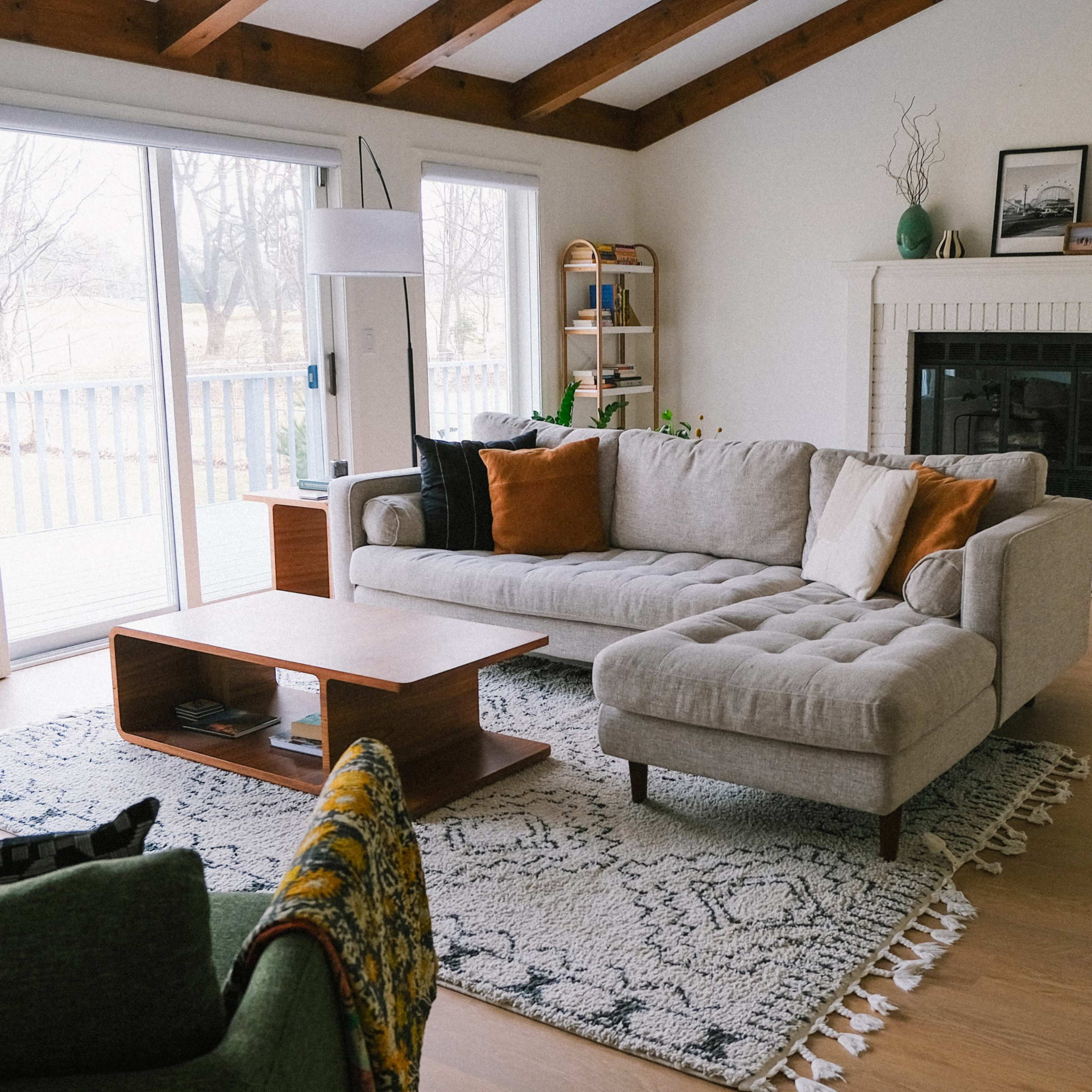 A spacious living room features a light gray sectional sofa with orange pillows, a wooden coffee table, and a guitar leaning against the wall next to a fireplace.