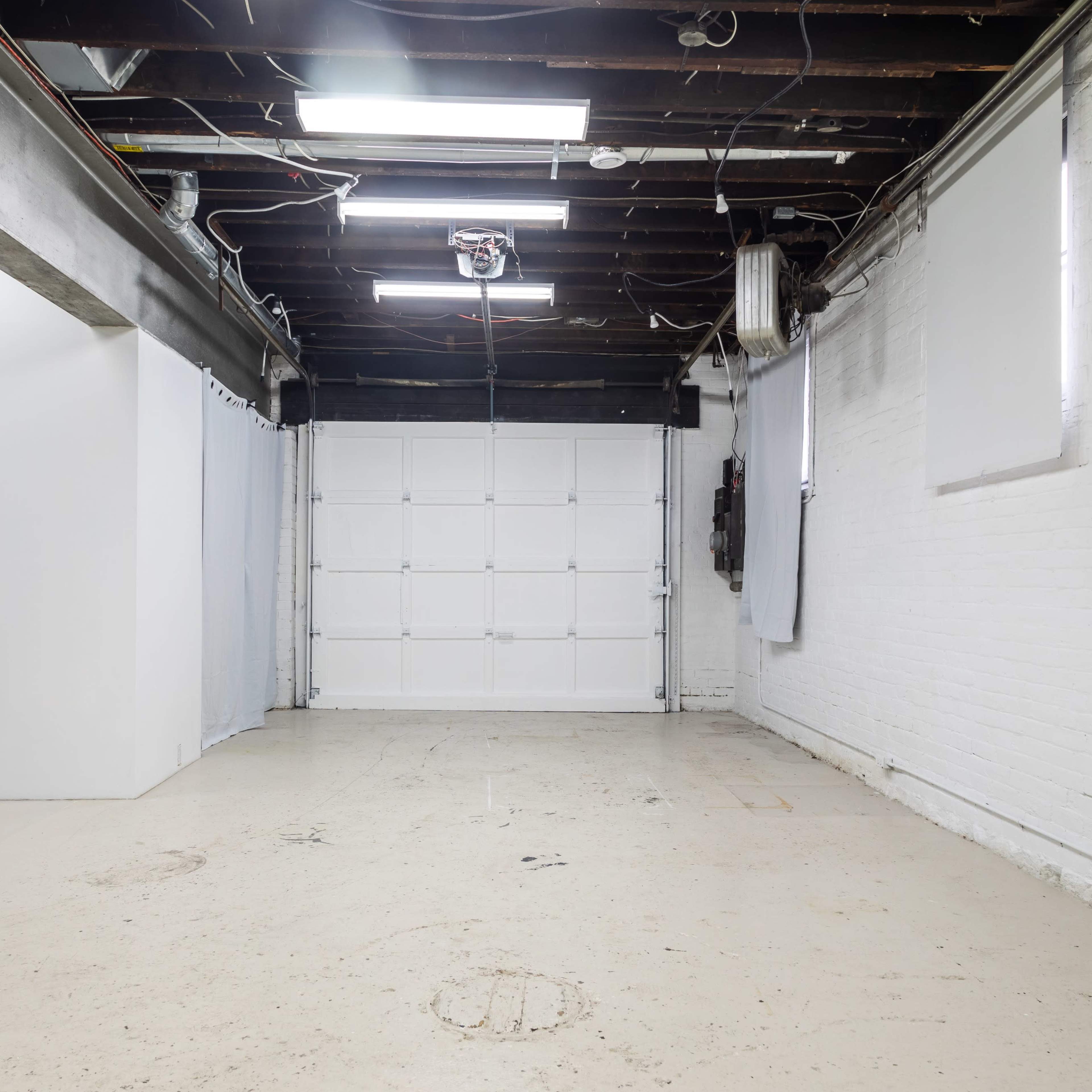 A vacant interior space with exposed beams and a large garage door at one end.