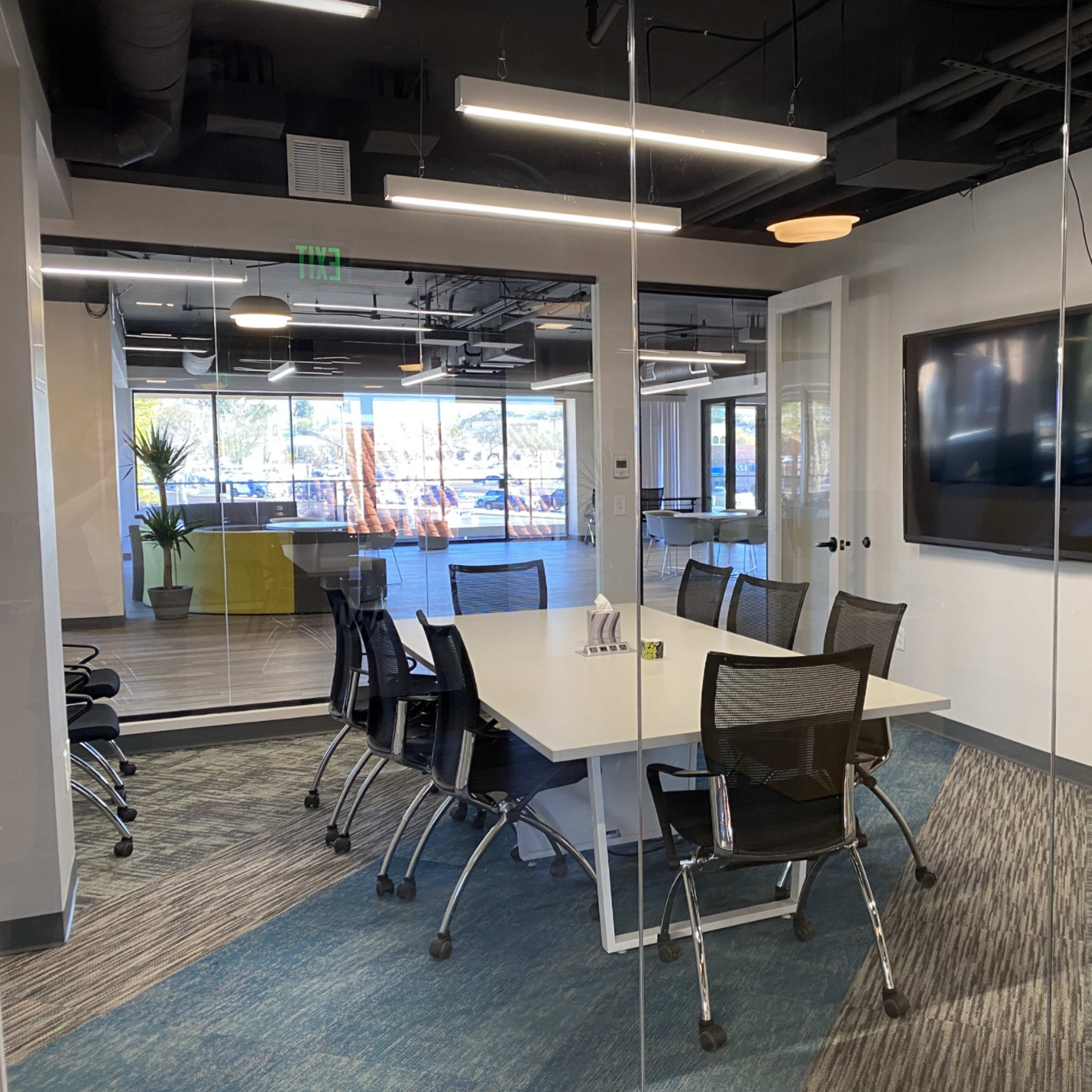 A glass-walled conference room equipped with a large table, chairs, and a flat-screen TV.