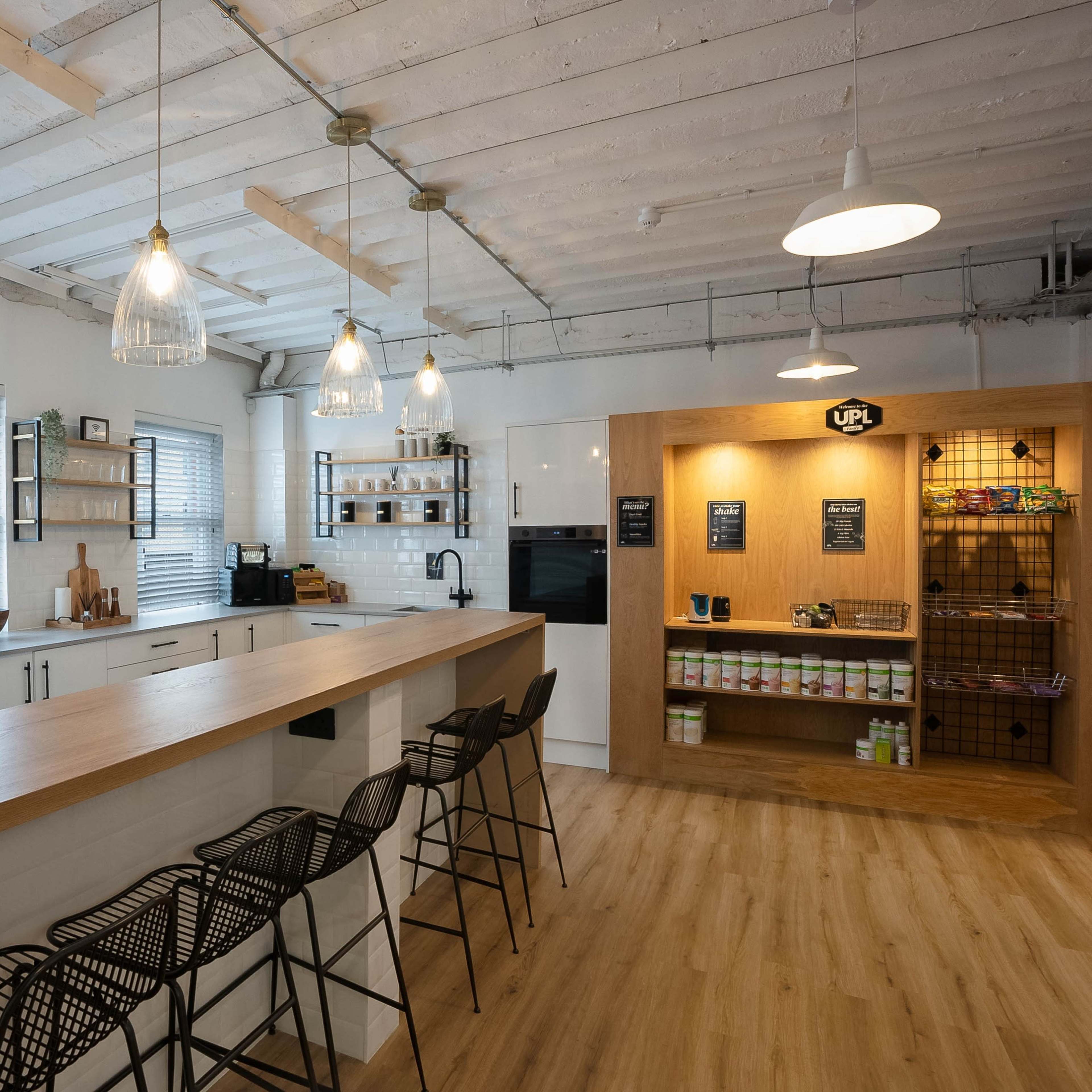A modern kitchen setting with a black refrigerator, a wooden island with bar stools, and shelves displaying various kitchen items and products.
