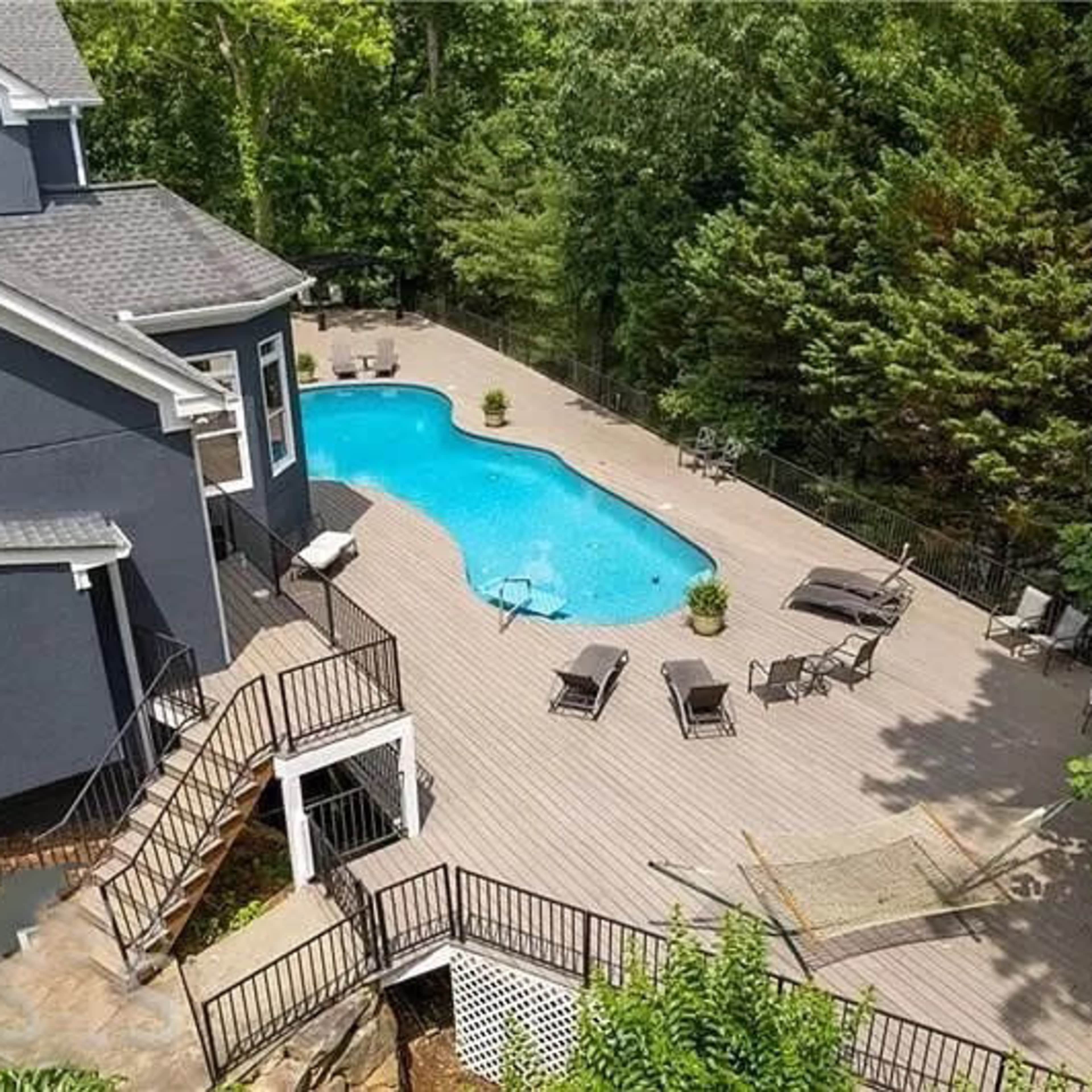 A modern home features a landscaped pool area surrounded by a wooden deck and lounge chairs.