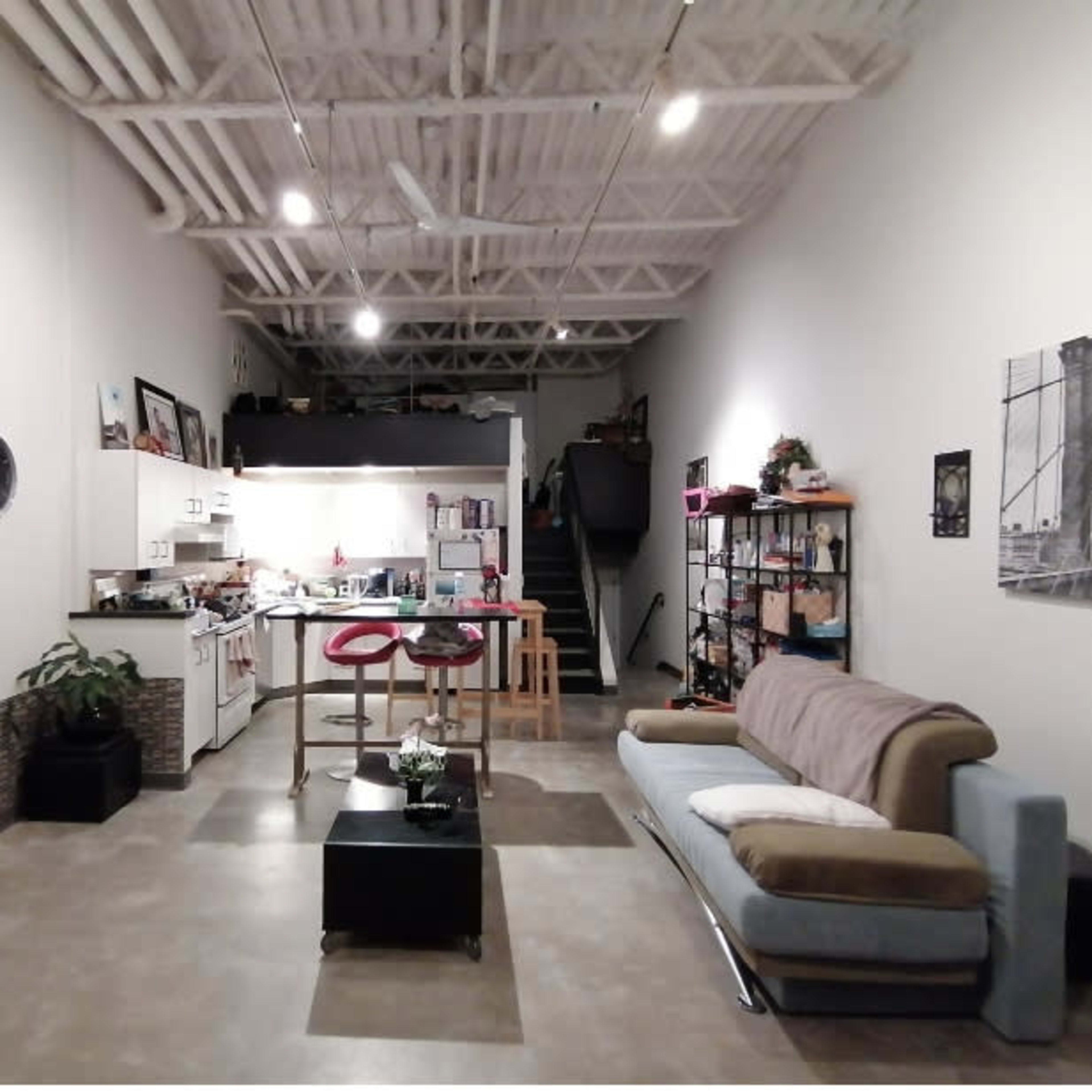 A spacious, modern open-concept living area with a kitchen, dining table, and a living room featuring a sofa and a television.