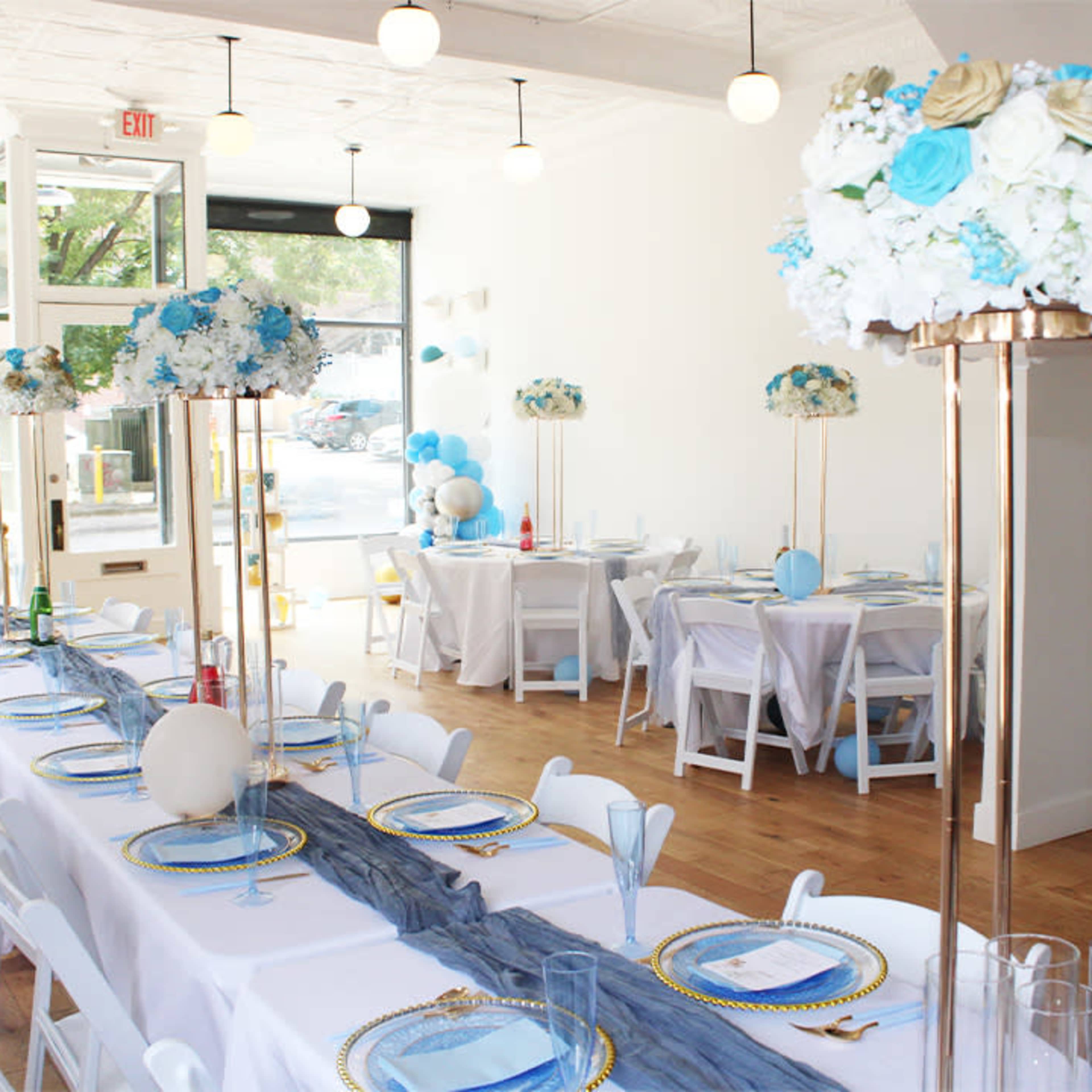 A styled event space features long tables adorned with blue and white floral centerpieces under modern lighting.