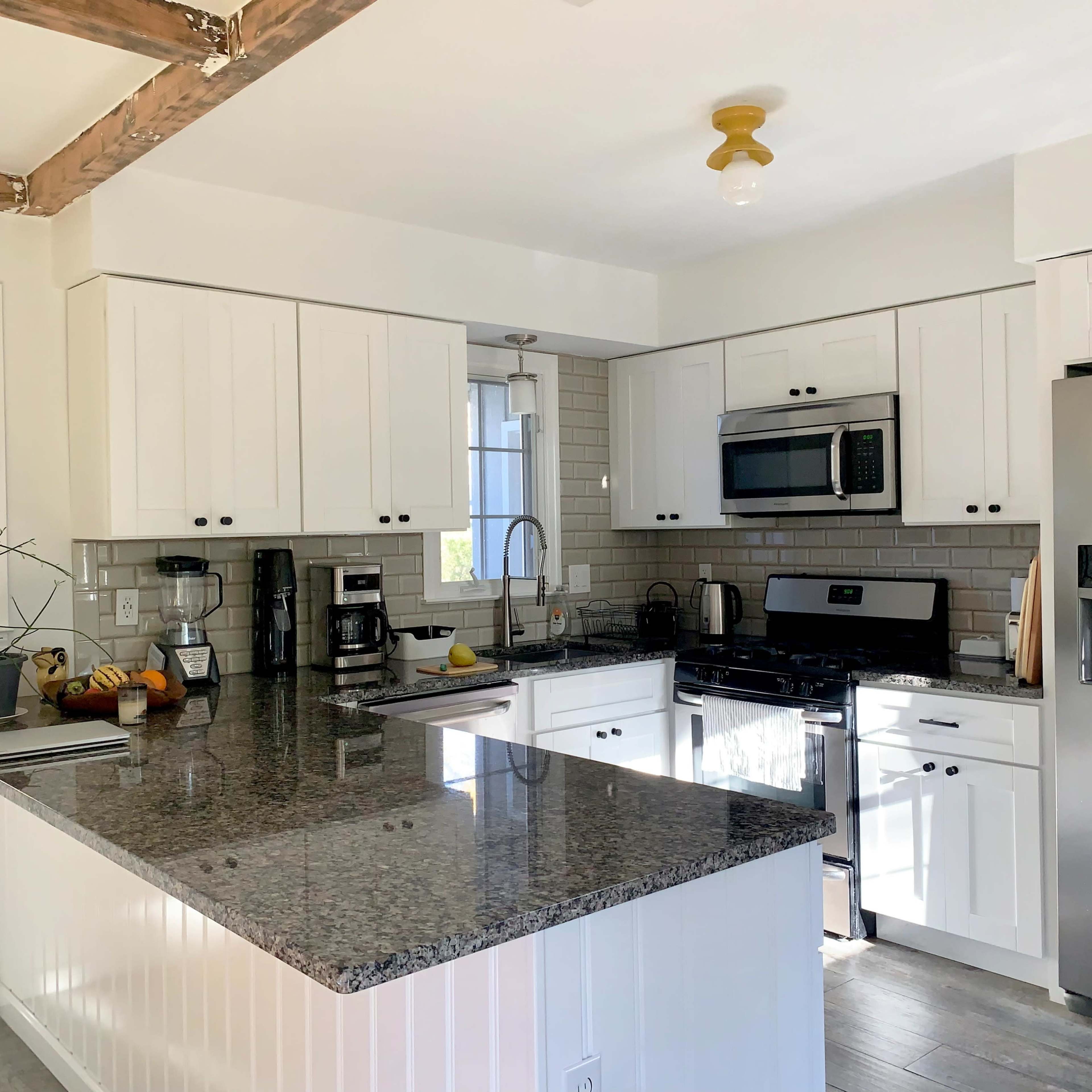 A modern kitchen featuring white cabinets, a granite countertop, stainless steel appliances, and a window with natural light.