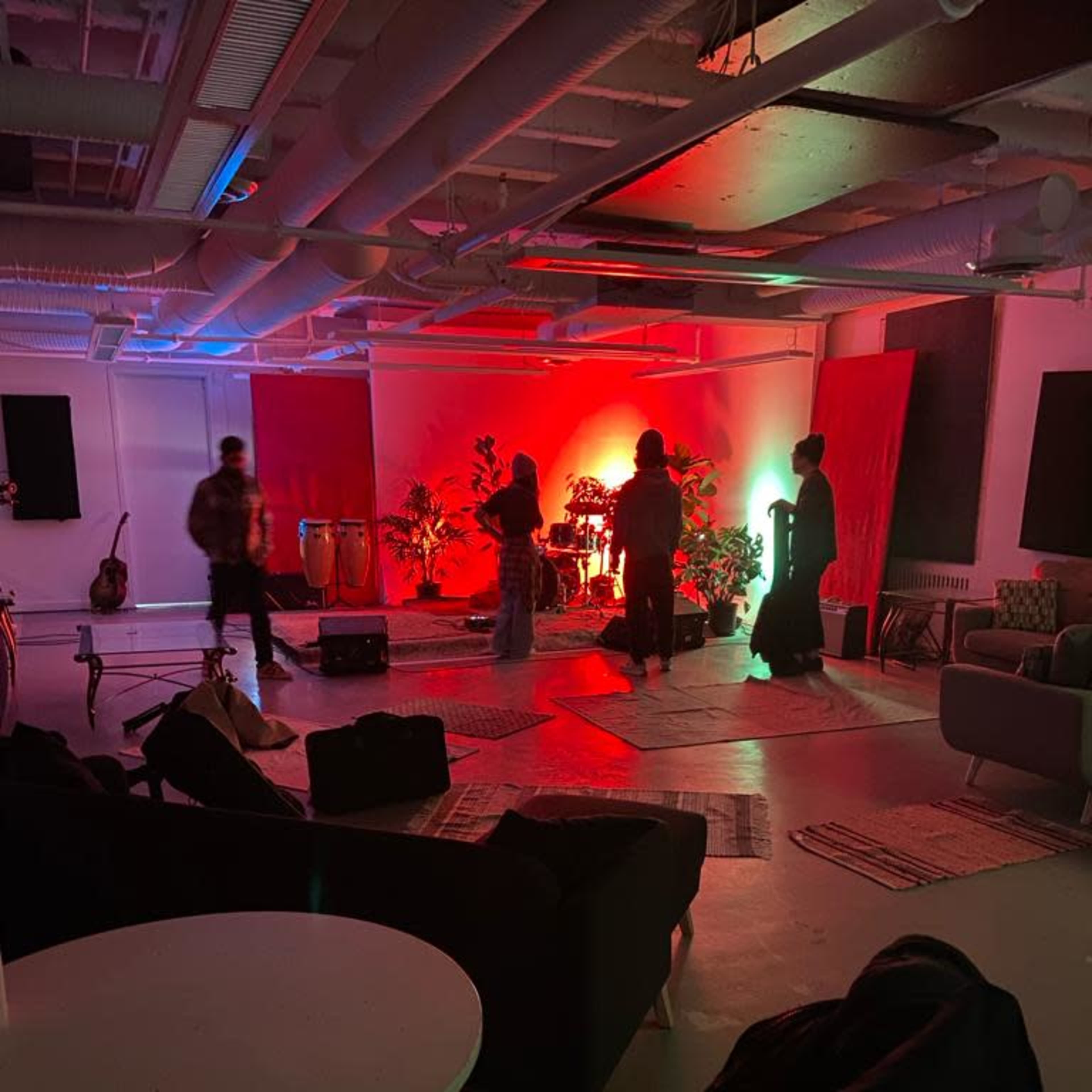 Musicians set up on a stage in a dimly lit room adorned with plants and musical instruments.