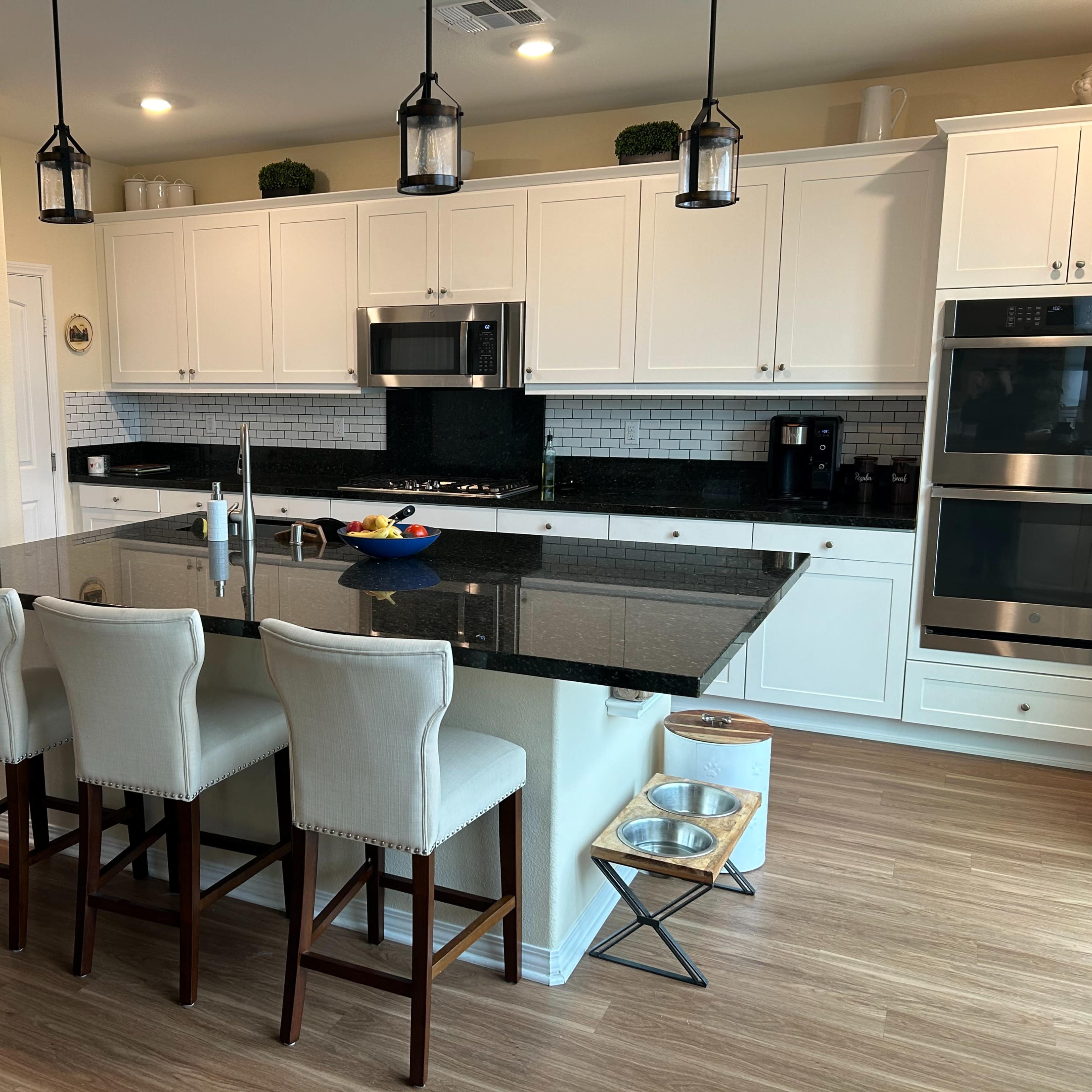 A modern kitchen with white cabinetry, a black granite island, and three upholstered stools.