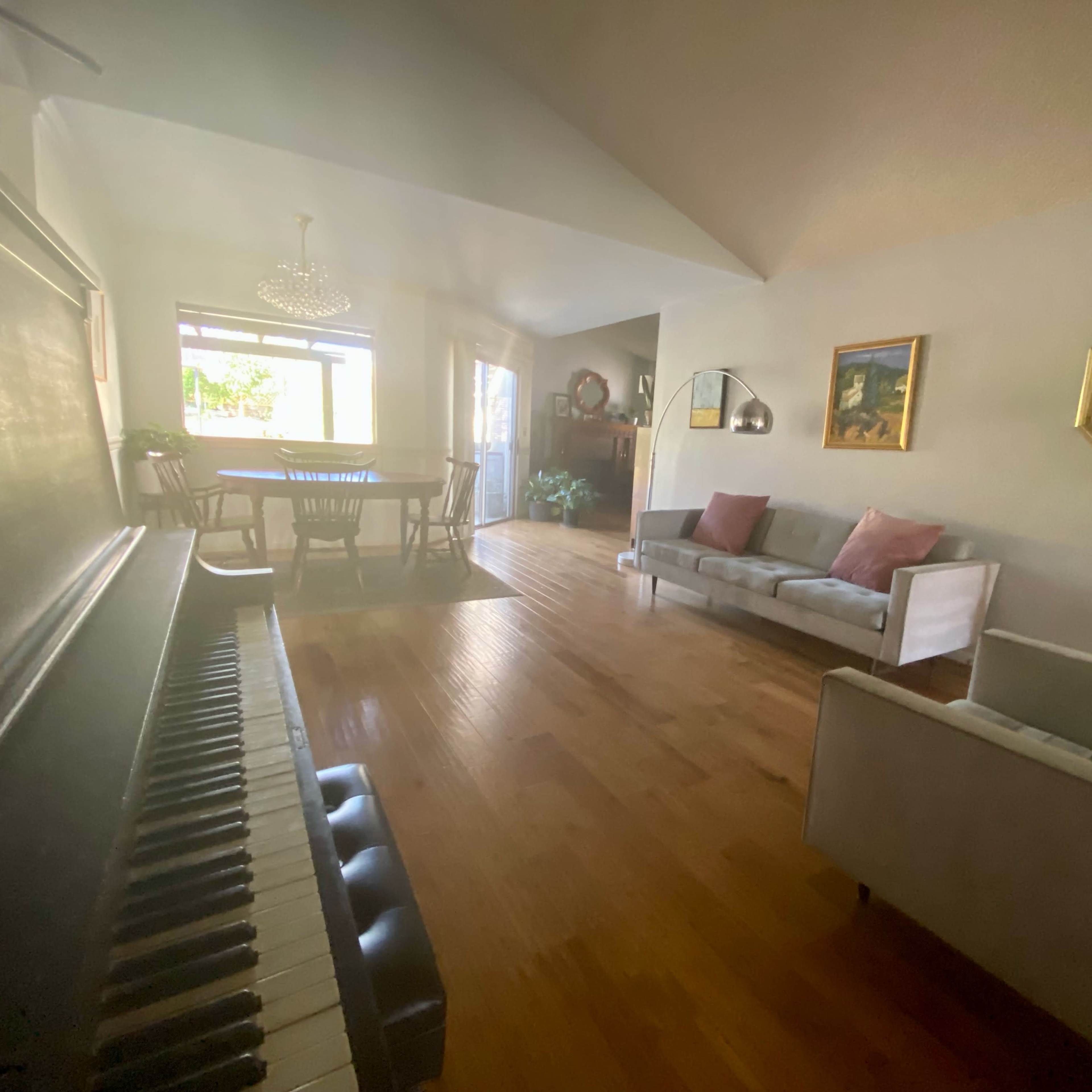 A living room with a piano on the left, a sofa and armchairs in the center, and a dining area visible in the background.