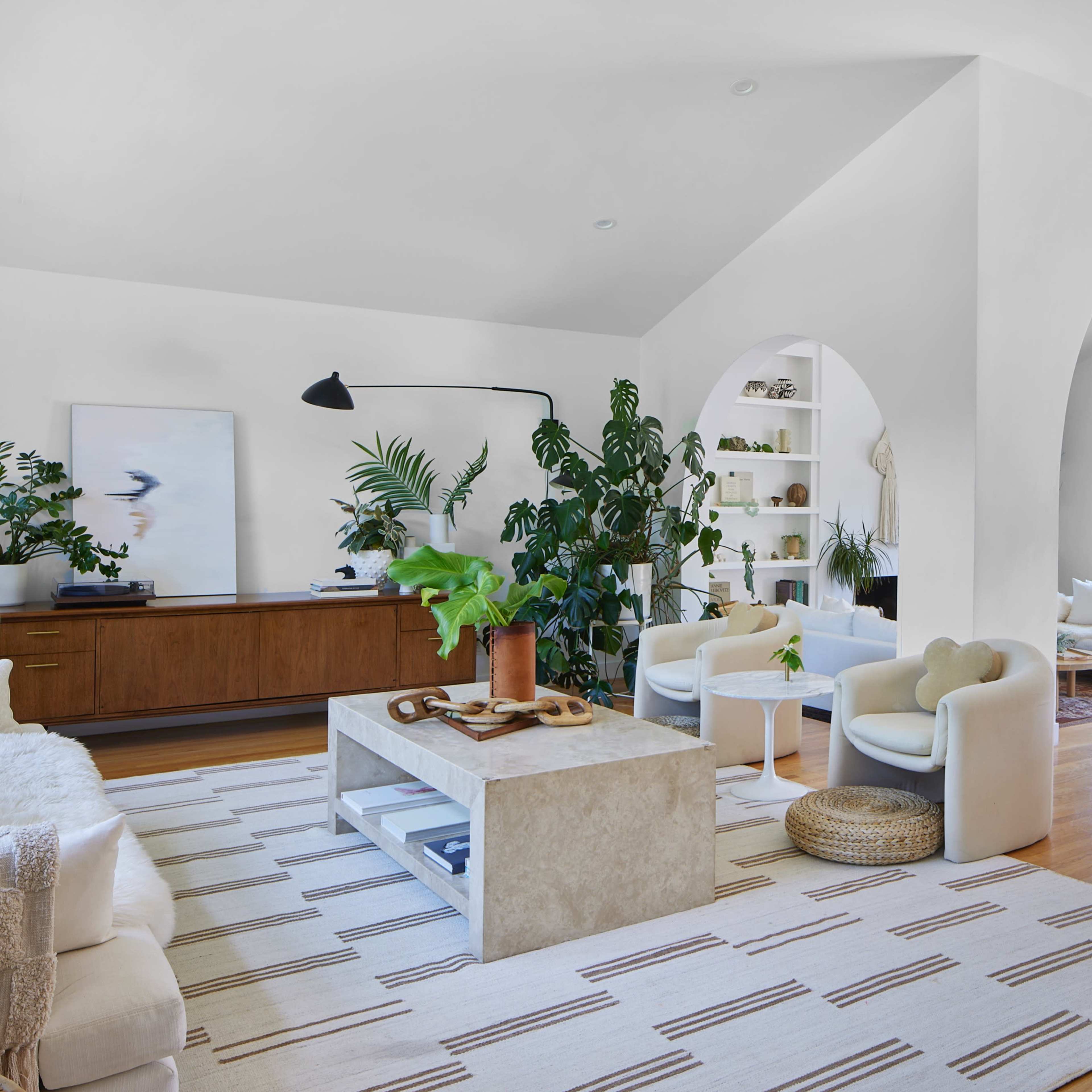 An open-concept living space with white walls, hardwood floors, and a combination of modern furnishings including a stone coffee table, circular armchairs, and a long dining table.