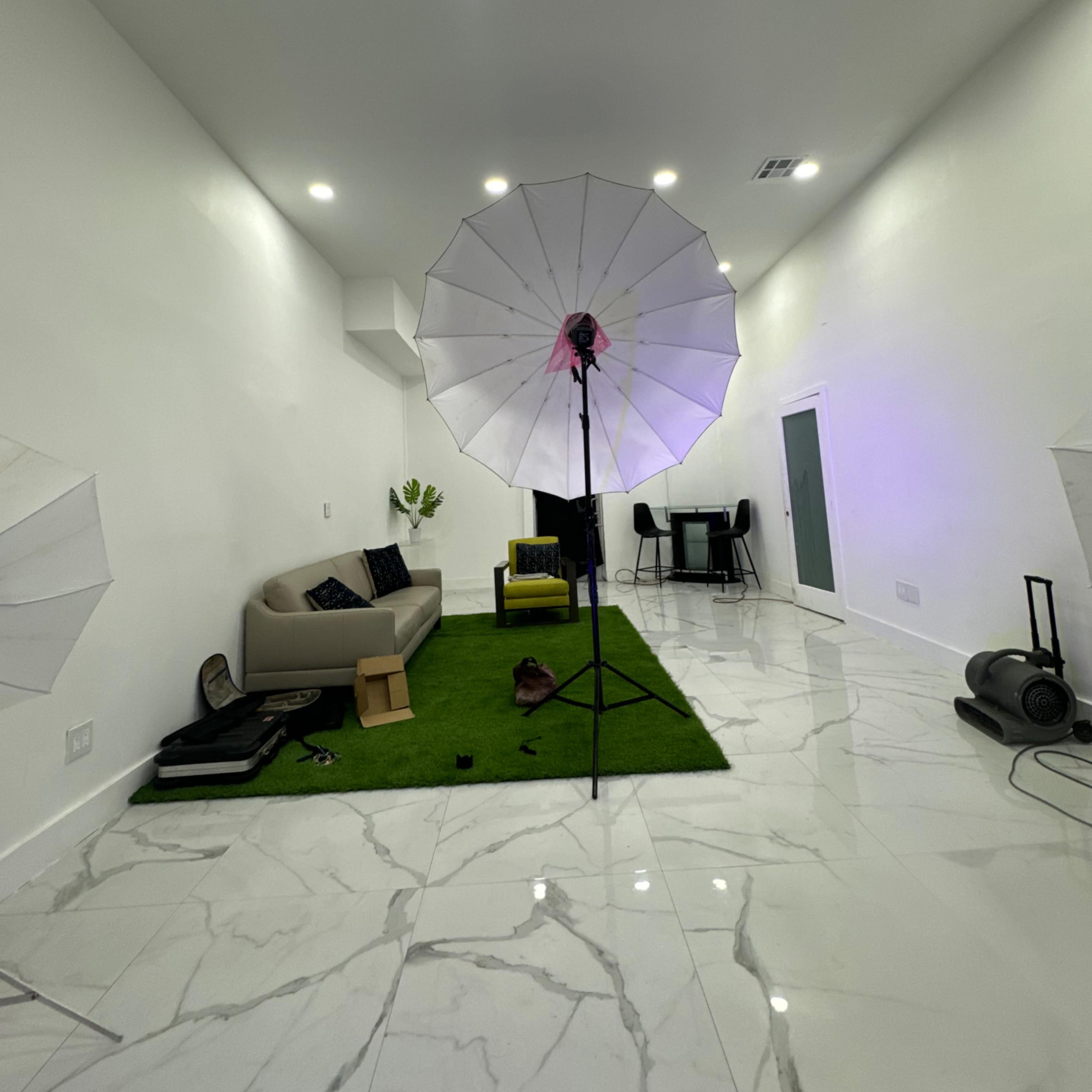 A spacious room with marble floors, two large light umbrellas set up, a green rug, a sofa, and a table in the background.