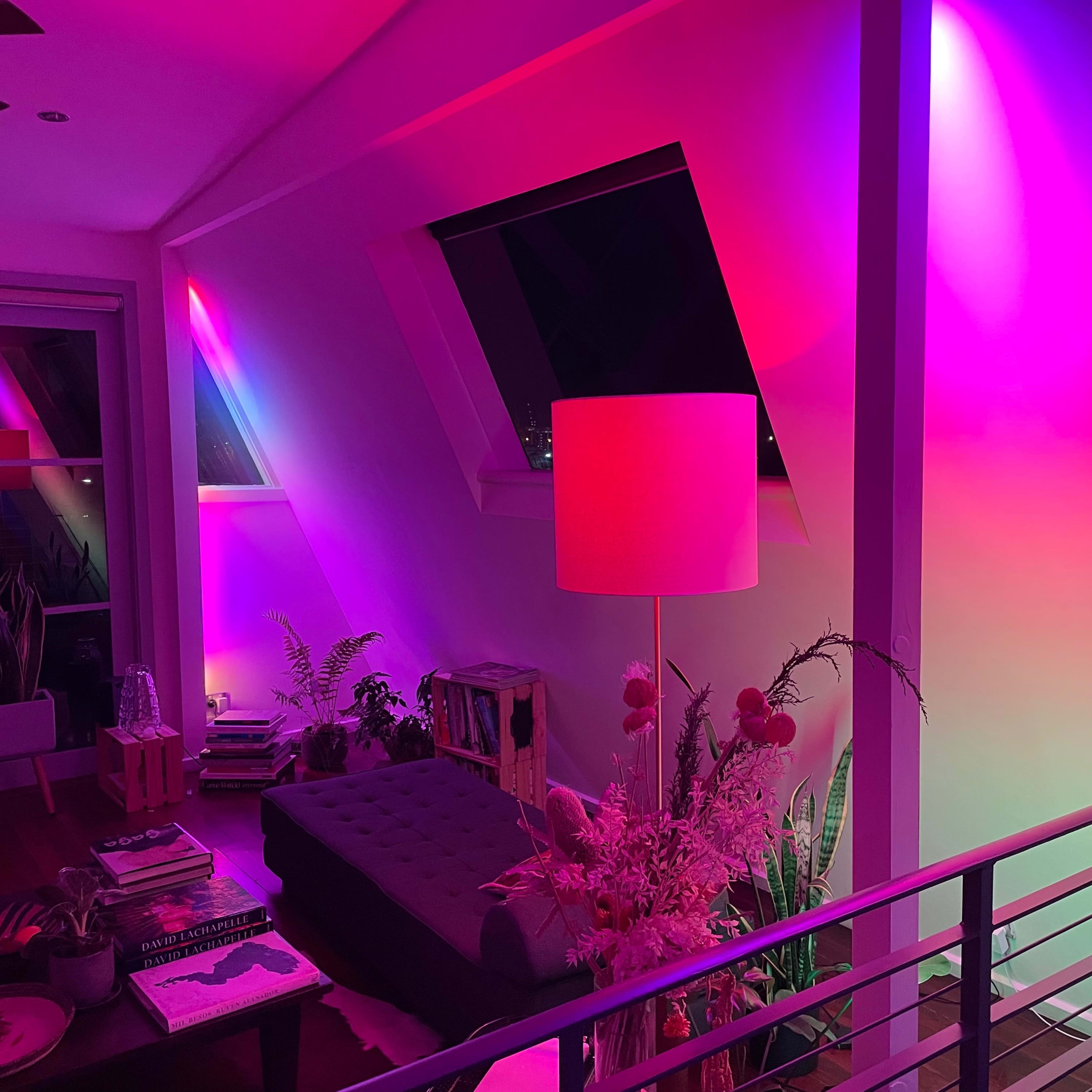 A modern living space features a sofa, a lamp, and vibrant pink and purple lights illuminating the walls and ceiling.