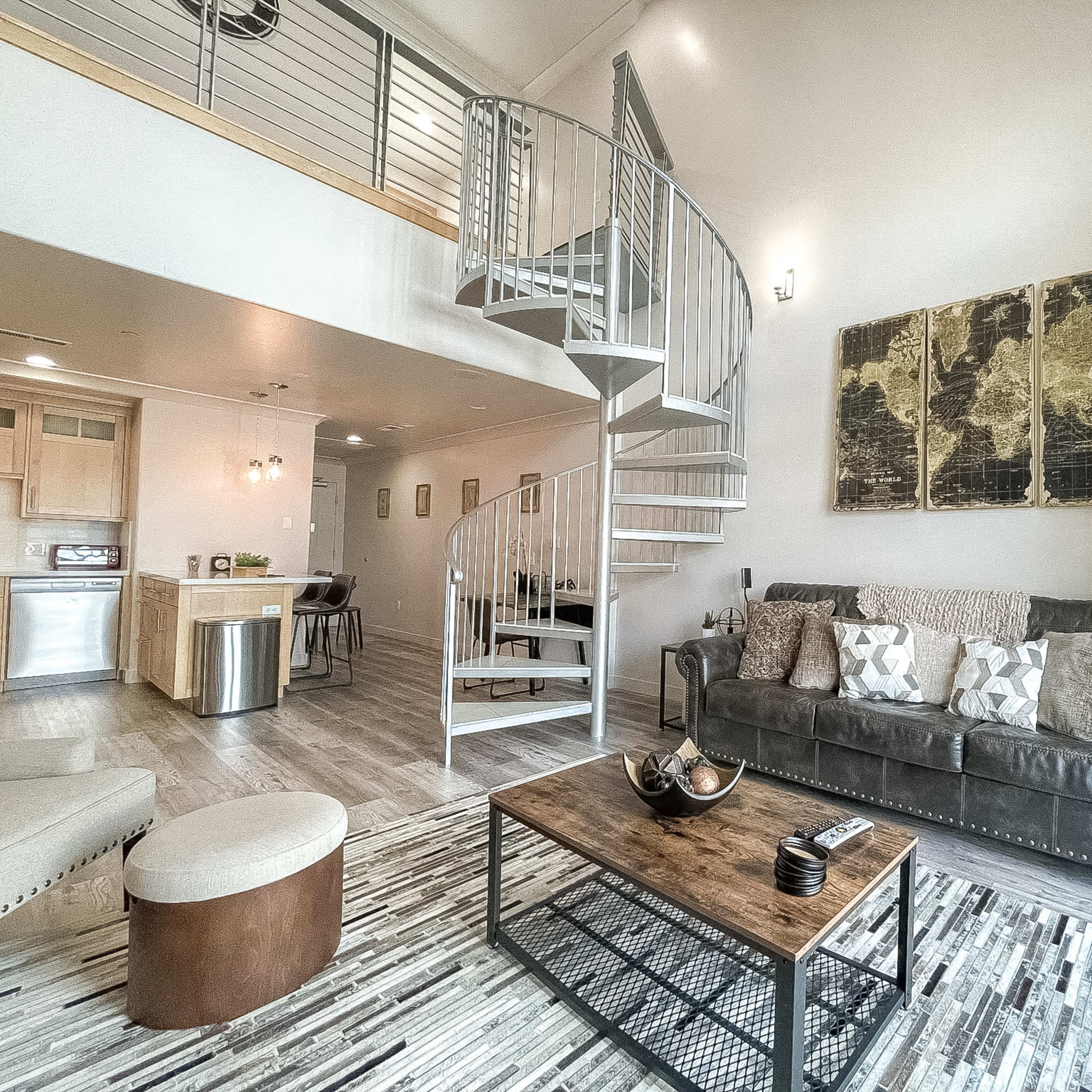 A modern living room featuring a leather sofa, a coffee table, and a spiral staircase leading to a loft area.