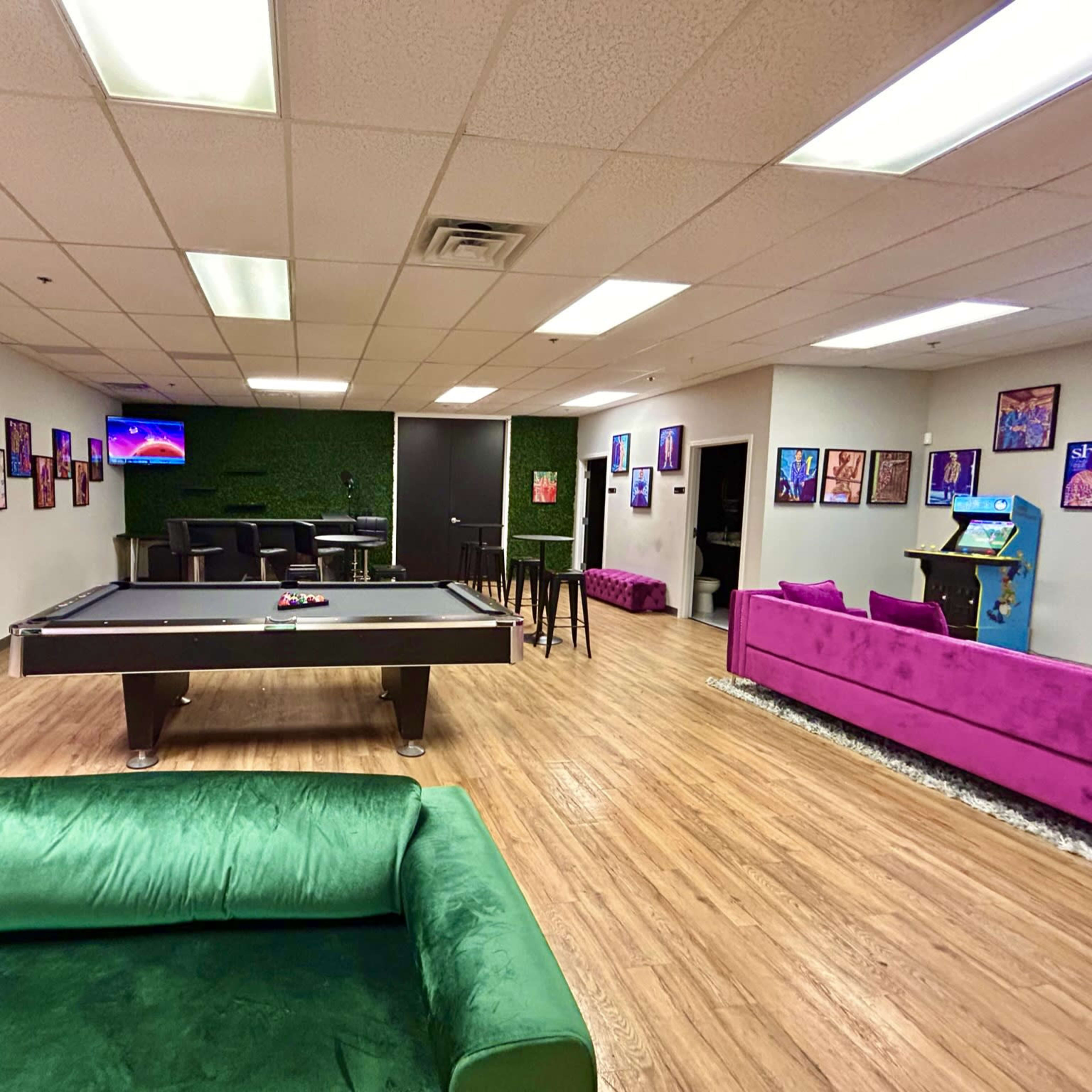 A recreational room with a pool table, green couch, purple seating, and colorful artwork on the walls.