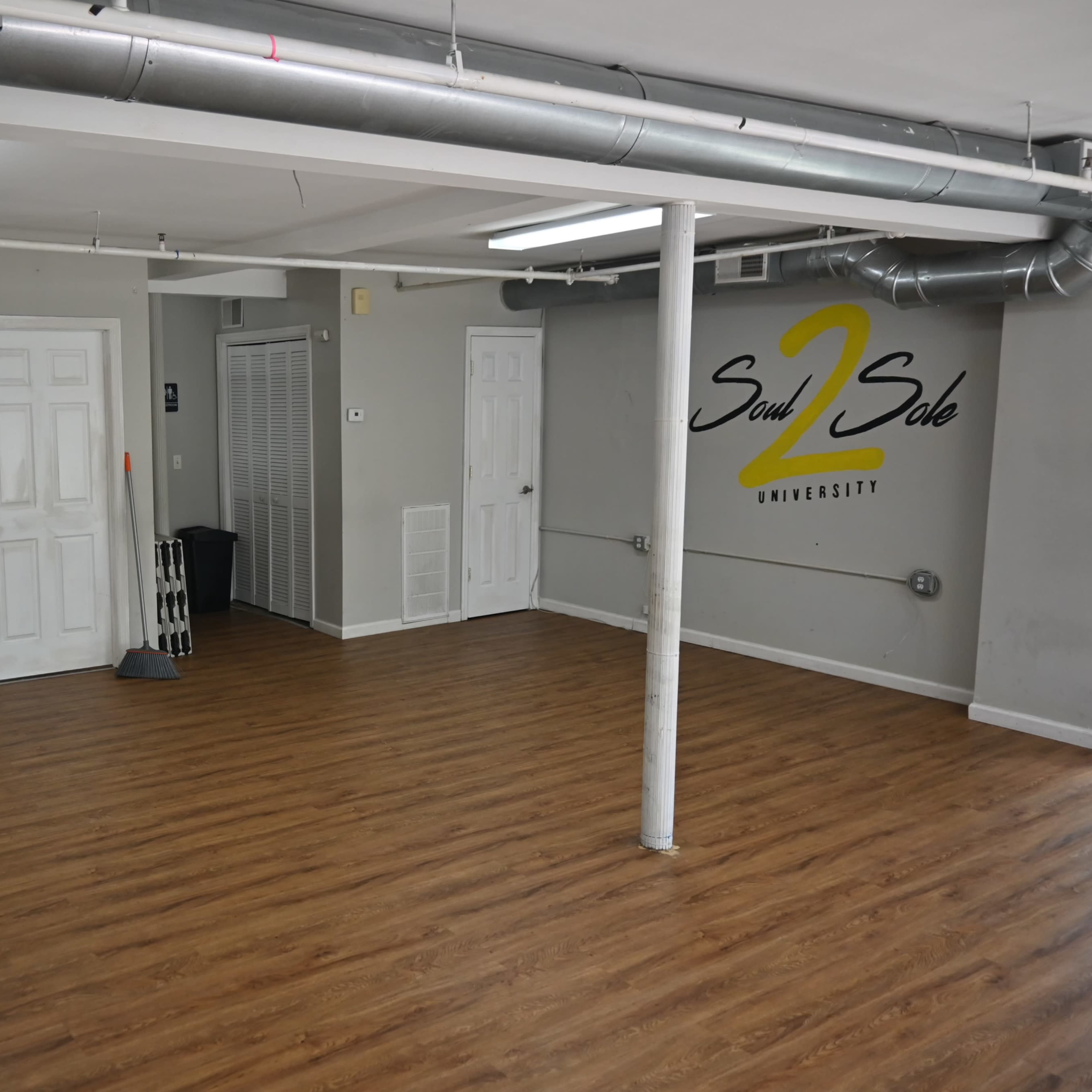 An empty room with wooden flooring, a white ceiling, and gray walls featuring the logo "Soul 2 Sole University."