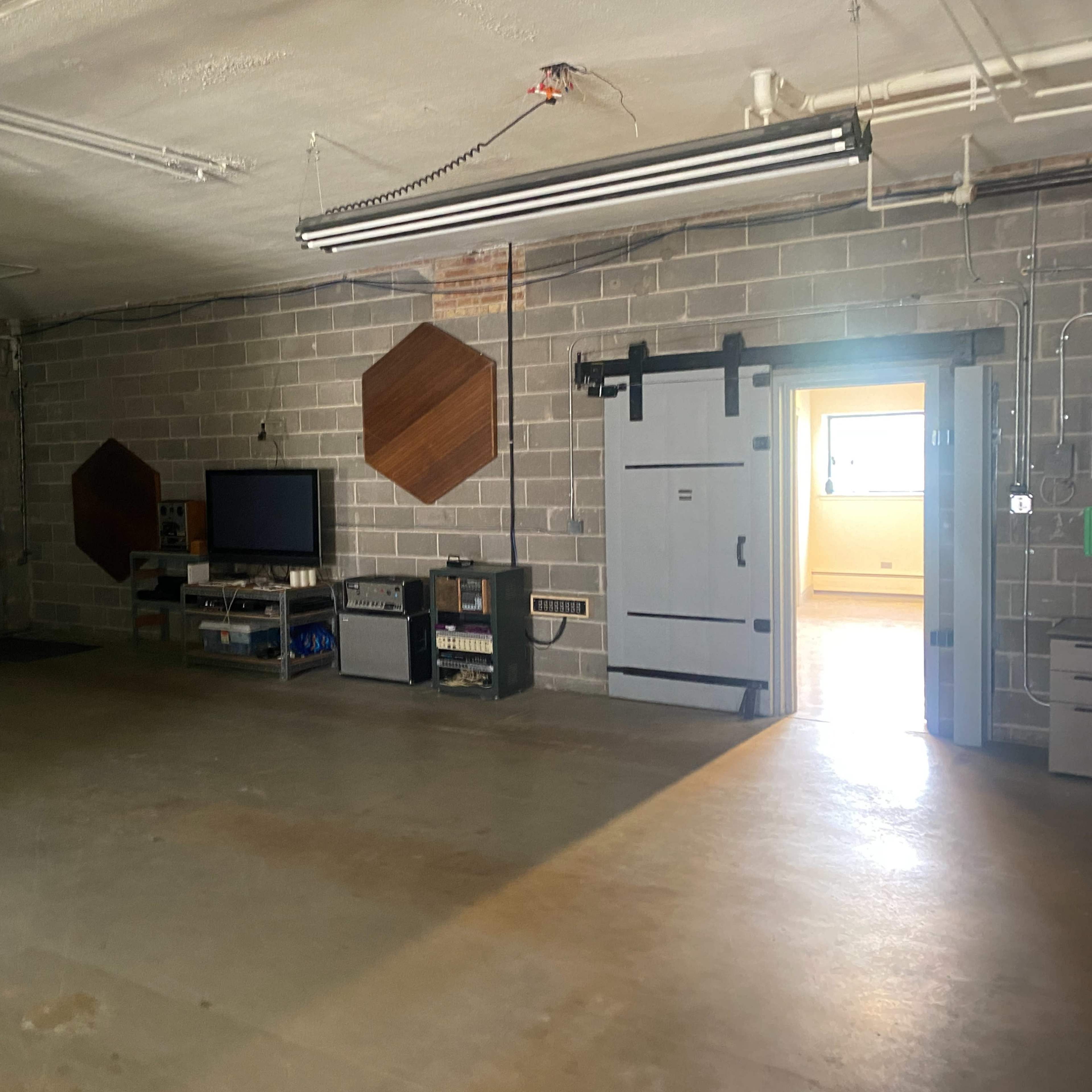 An empty industrial-style room with concrete walls, a television on a stand, and a doorway leading to another space.
