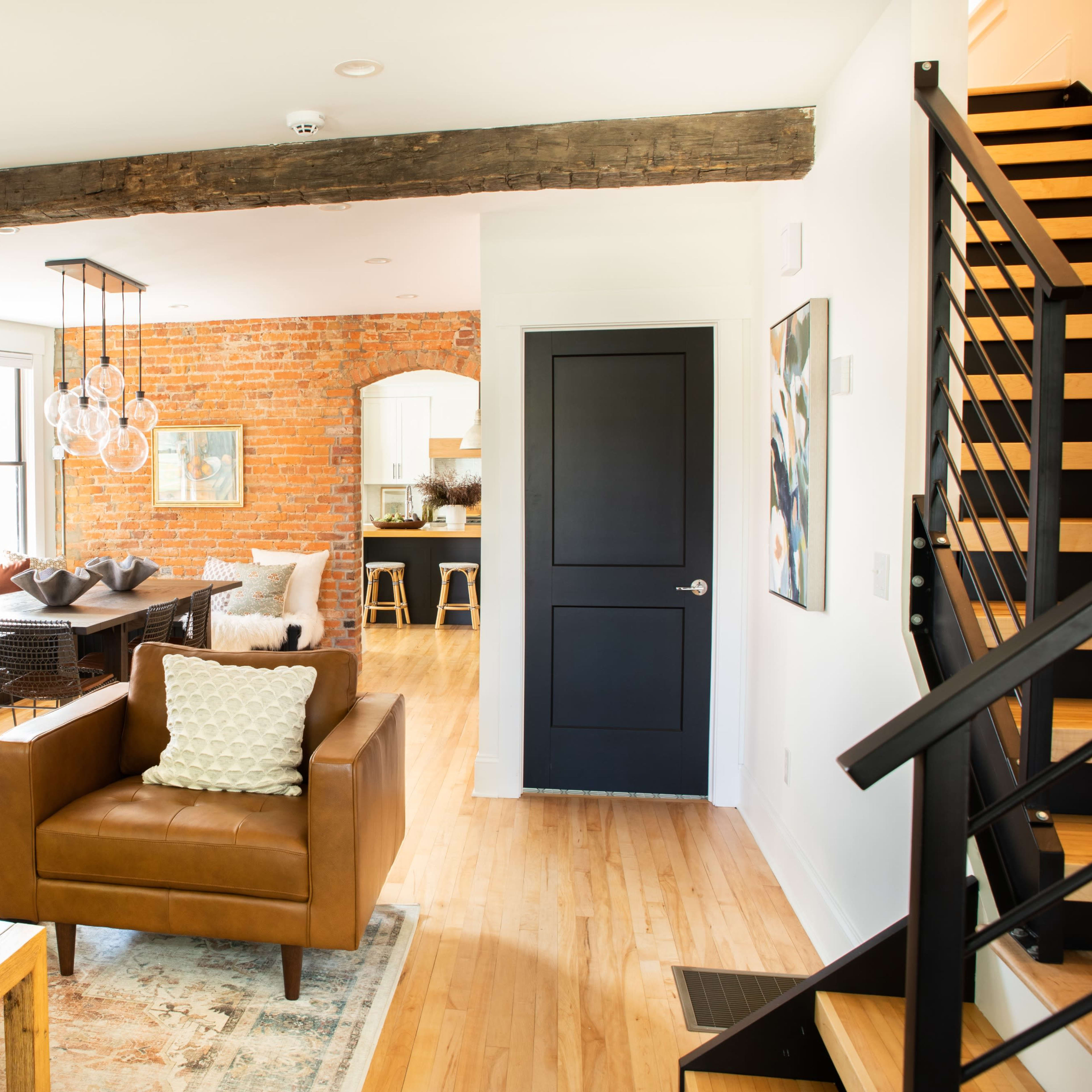 A modern living room with two brown leather chairs, a wooden beam across the ceiling, and a view of a dining area with a brick wall in the background.