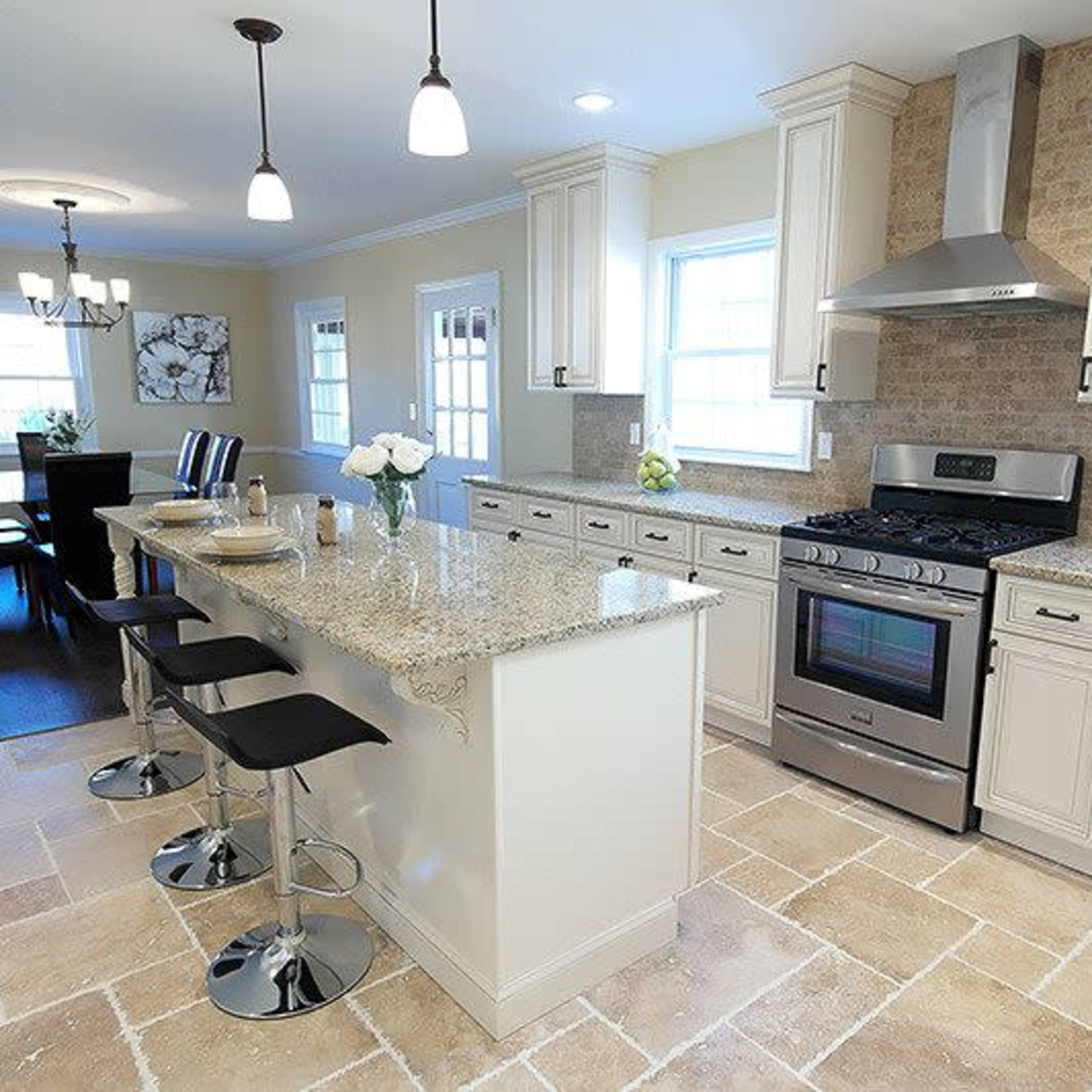 A modern kitchen features a central island with bar stools, stainless steel appliances, and light-colored cabinetry, adjacent to a dining area with a table and chairs.