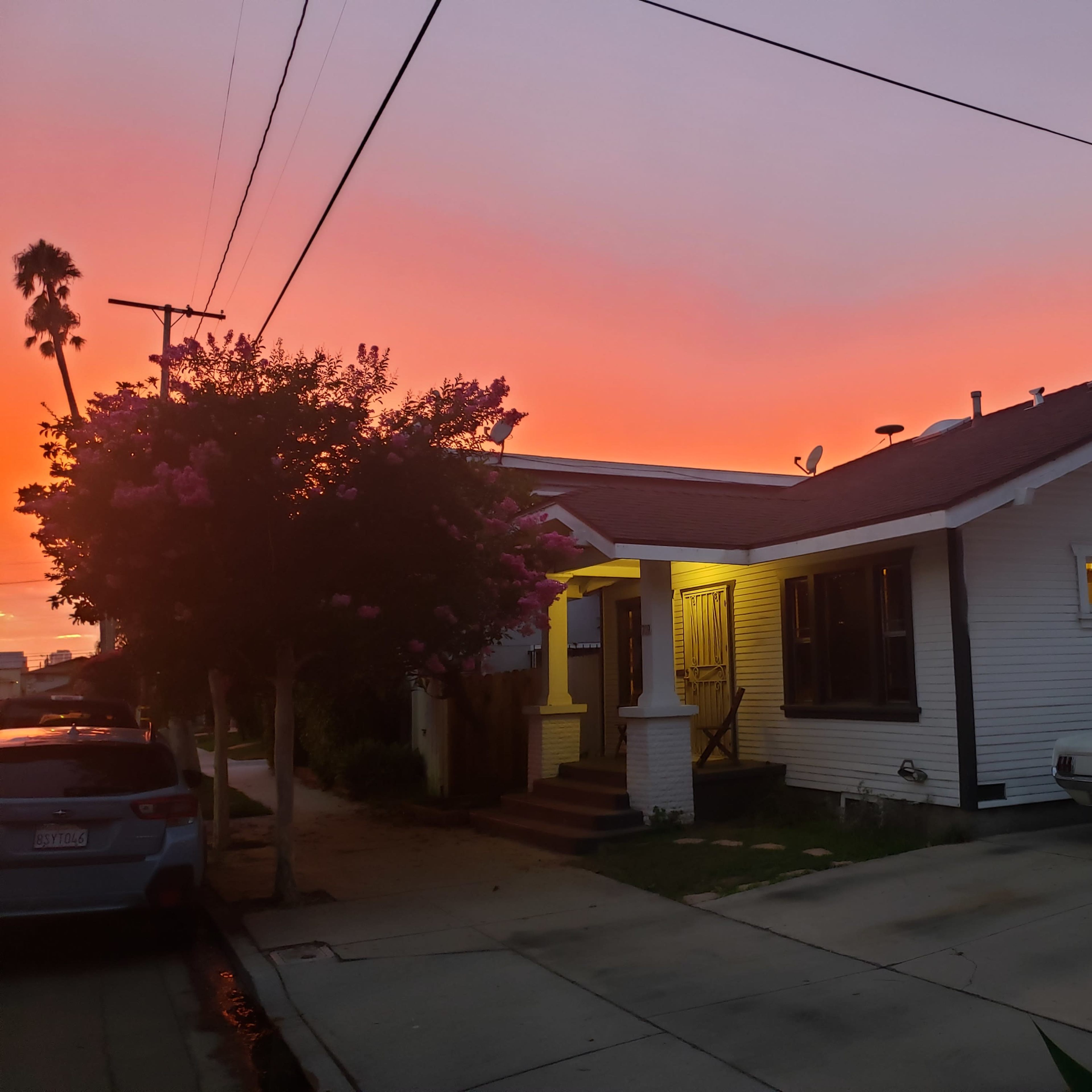 A white house with a red roof and a classic car is illuminated by a vibrant sunset.