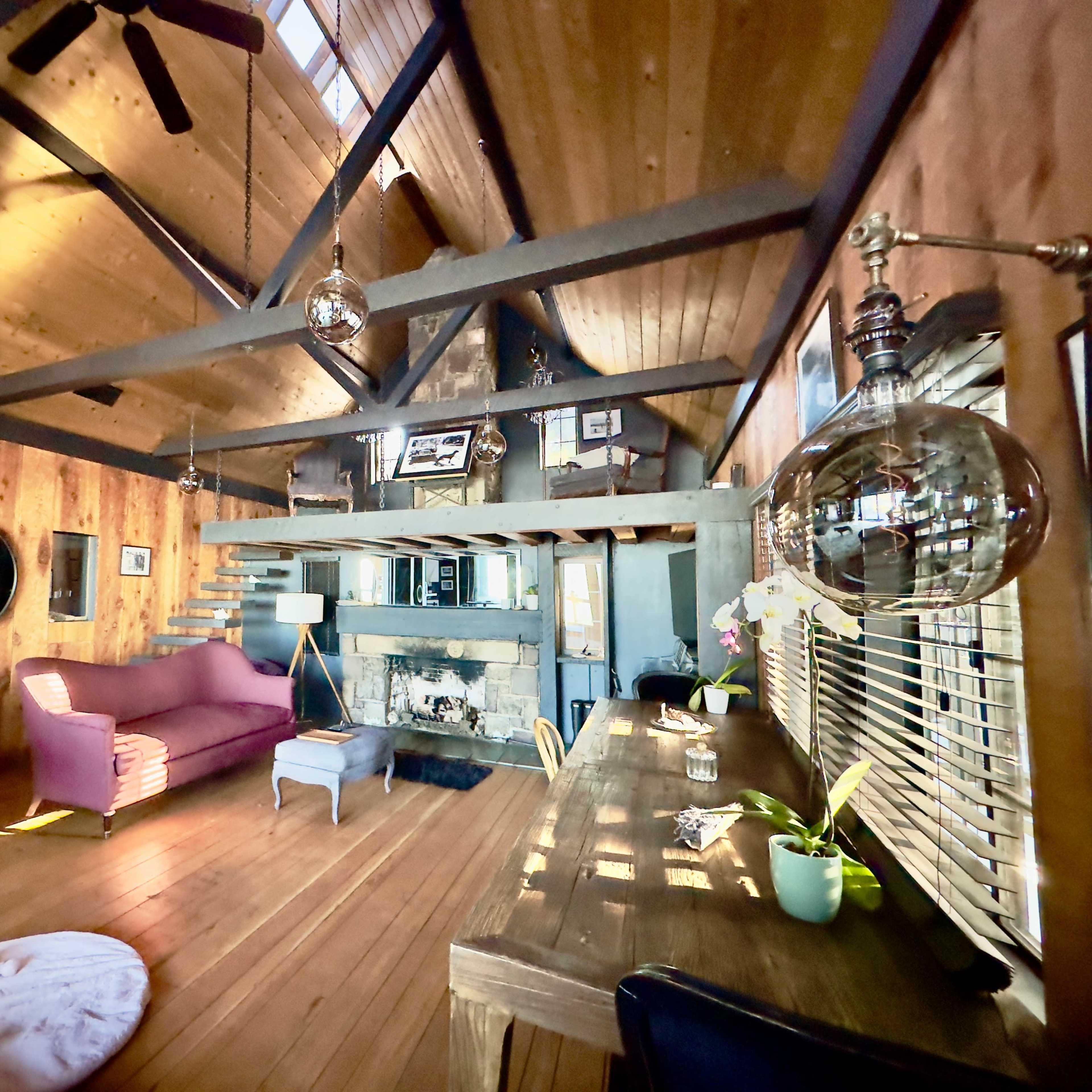 A rustic living space with wooden walls, a vaulted ceiling, a pink sofa, a wooden table, and a cozy fireplace.