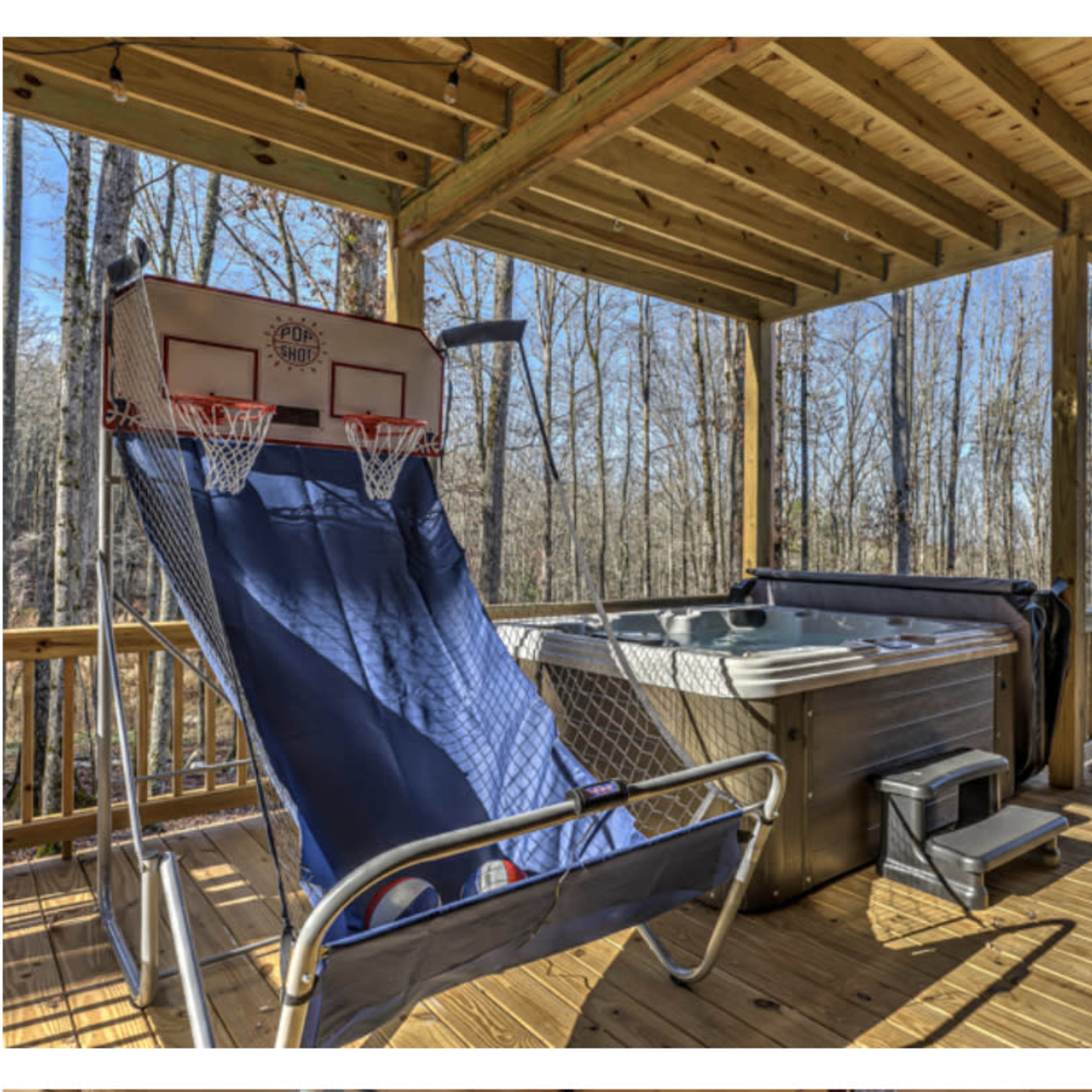 A wooden deck featuring a basketball hoop and a hot tub, surrounded by trees.