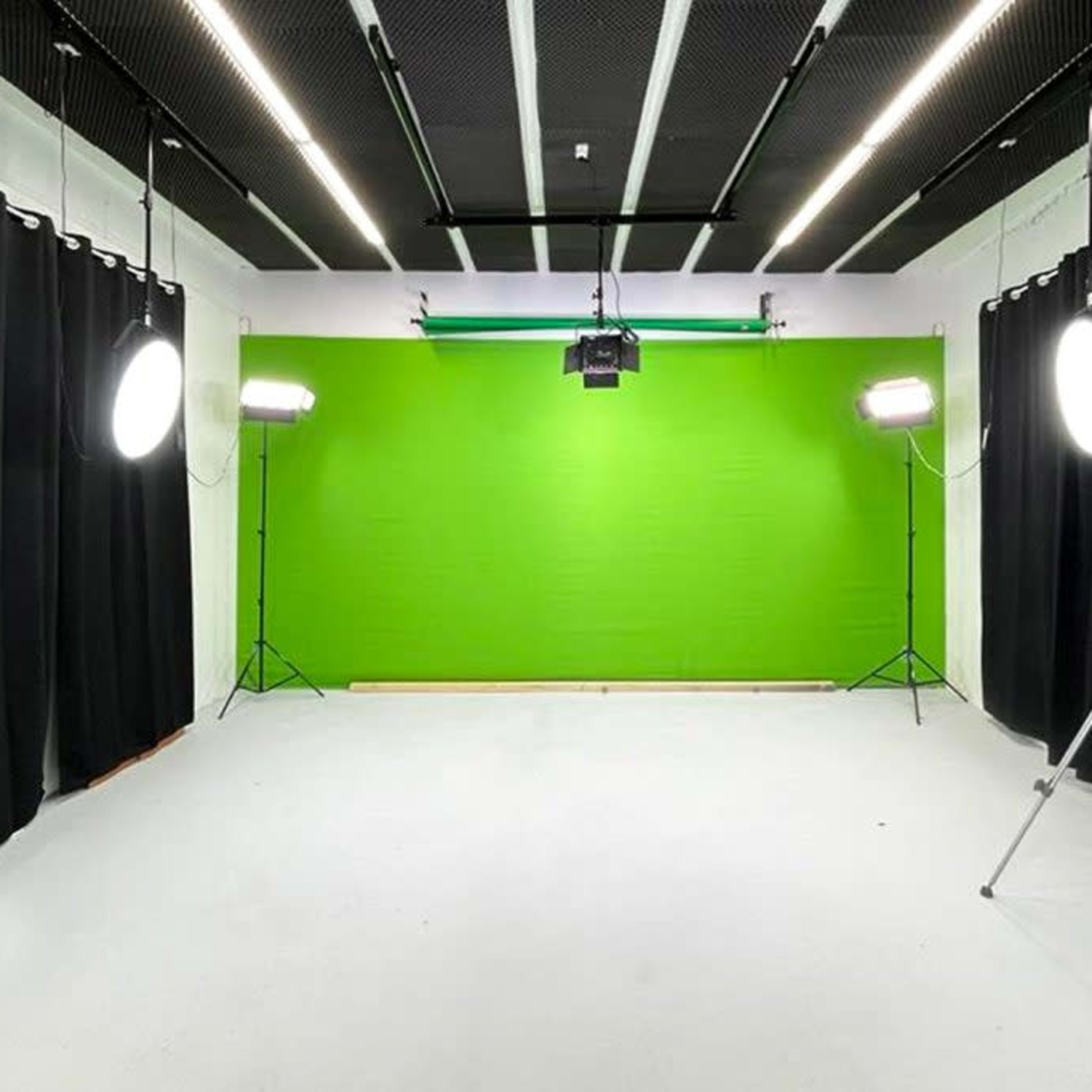 A brightly lit studio with a green backdrop, black curtains, and various lighting equipment.
