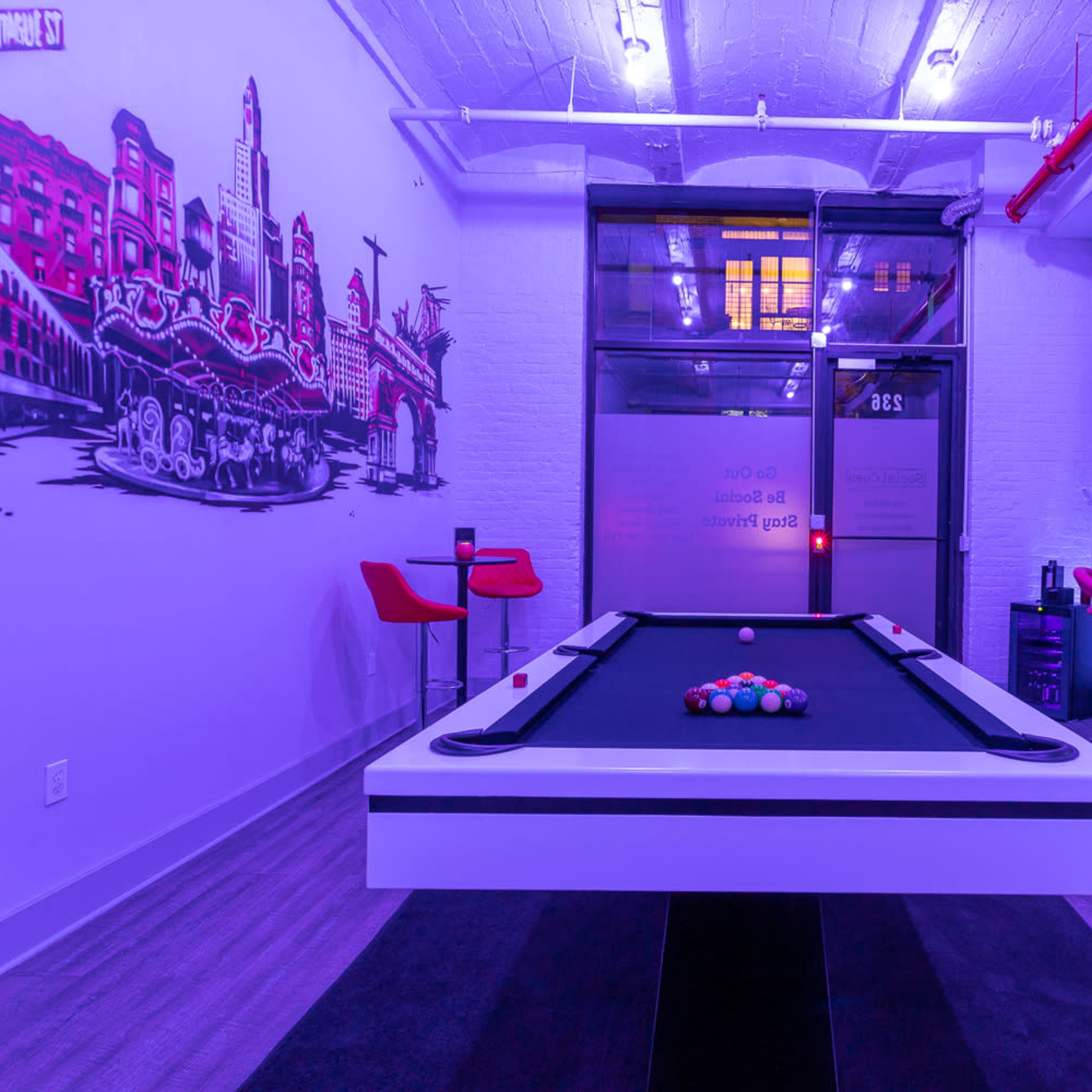 A modern pool table is centered in a brightly lit room featuring purple lighting and colorful wall art.