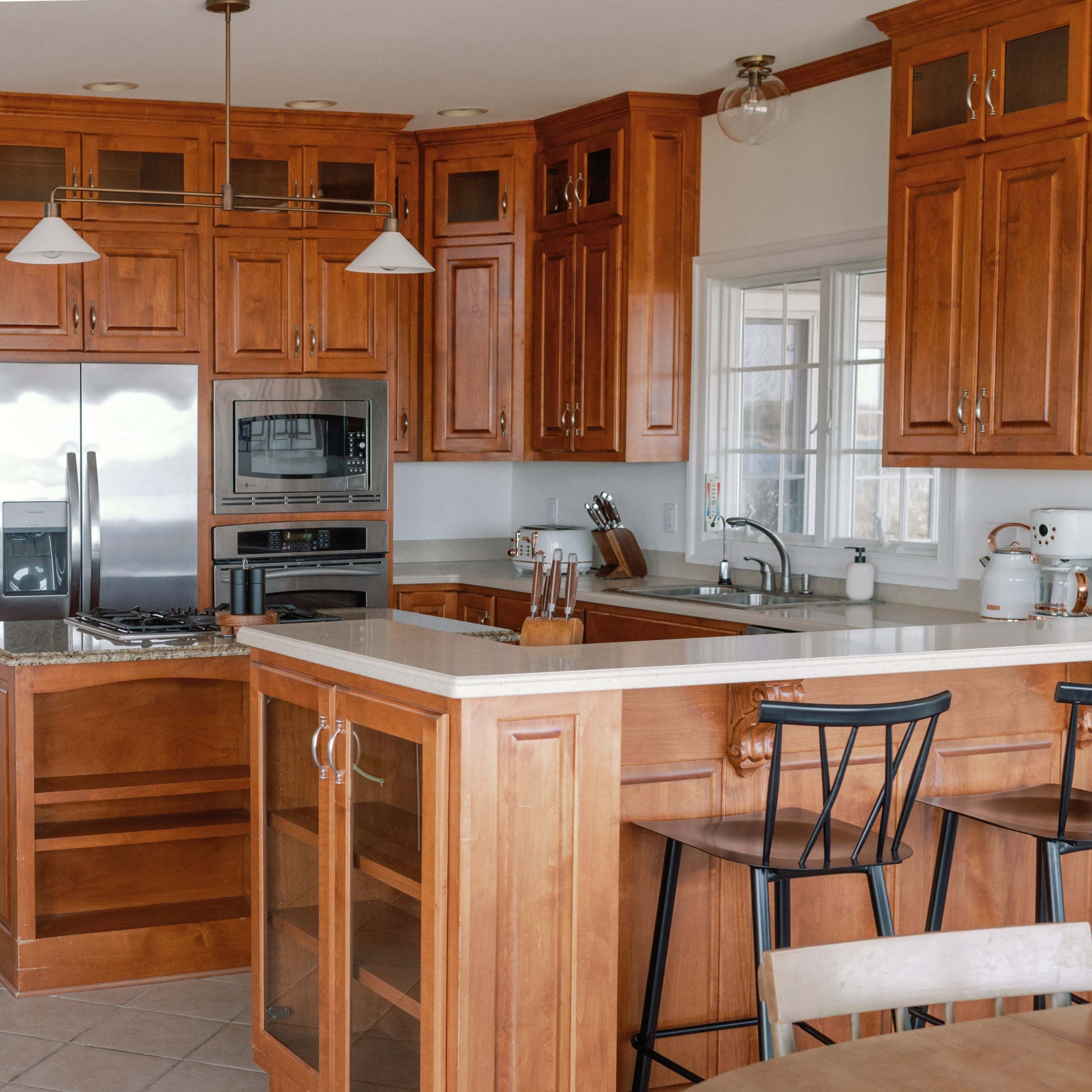 A modern kitchen featuring wooden cabinetry, stainless steel appliances, and a central island with bar stools.