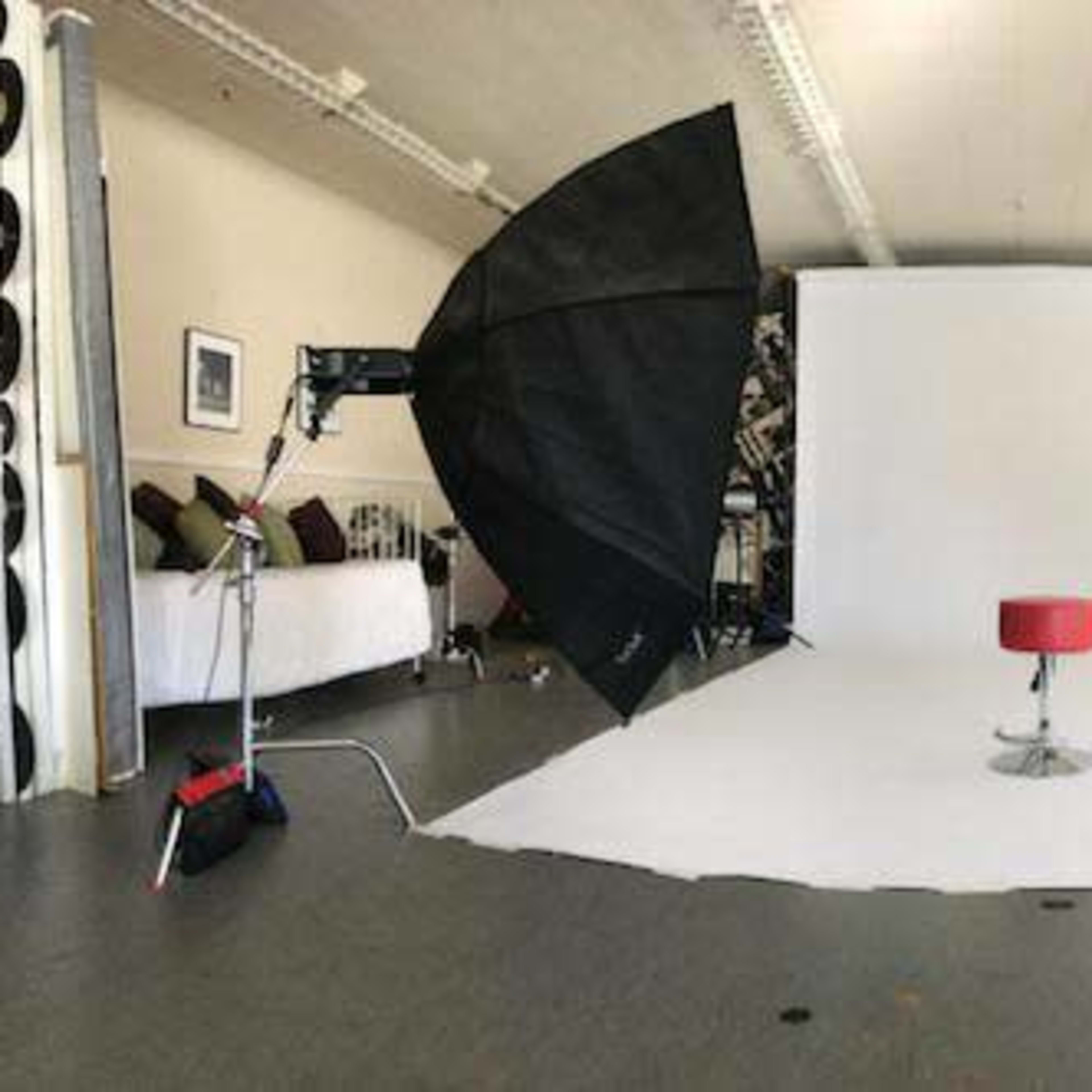 A photography studio setup with two large softbox lights, a small red stool in the center, and a blank white backdrop.