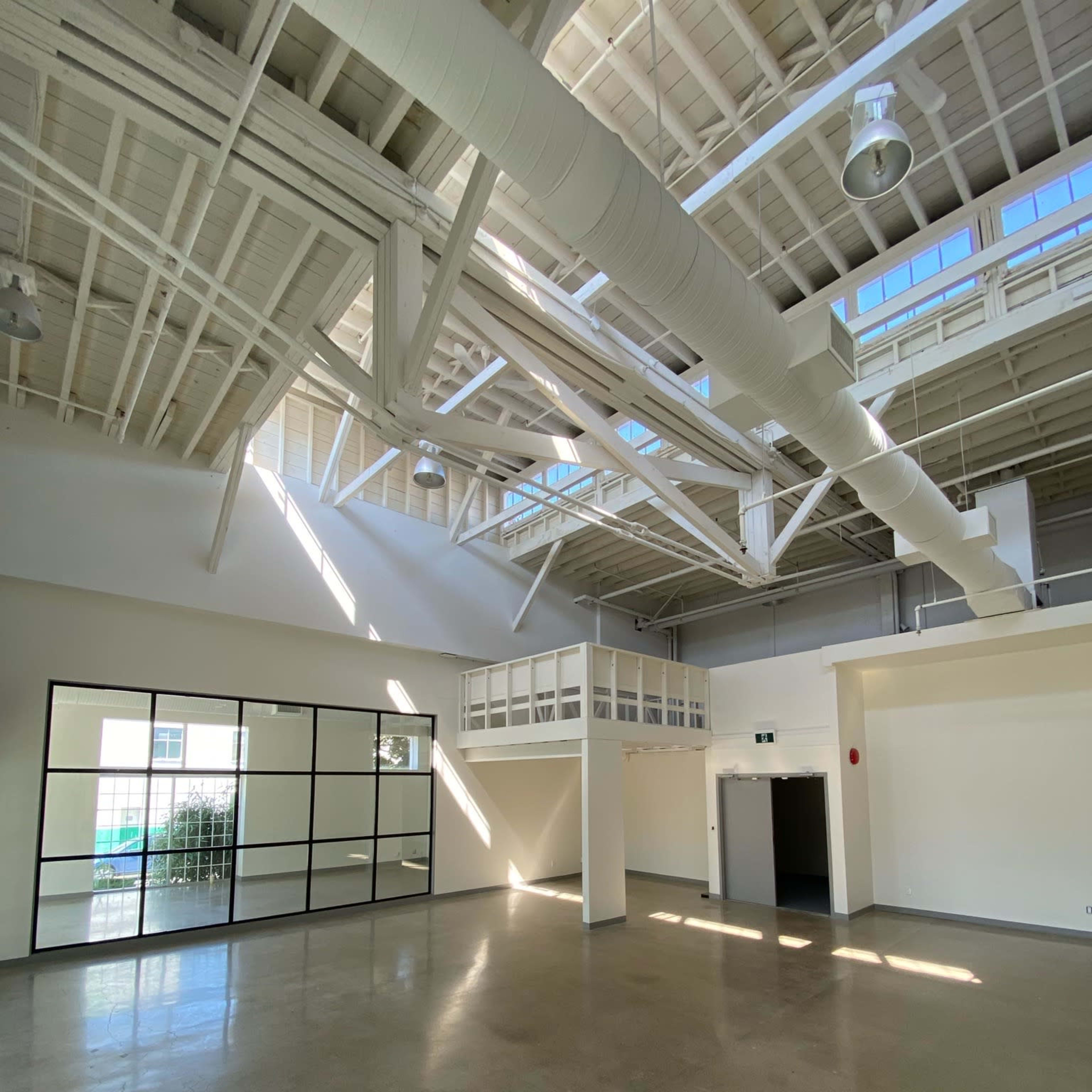 A spacious, well-lit interior with high ceilings, large windows, and a lofted area overlooking the main floor.